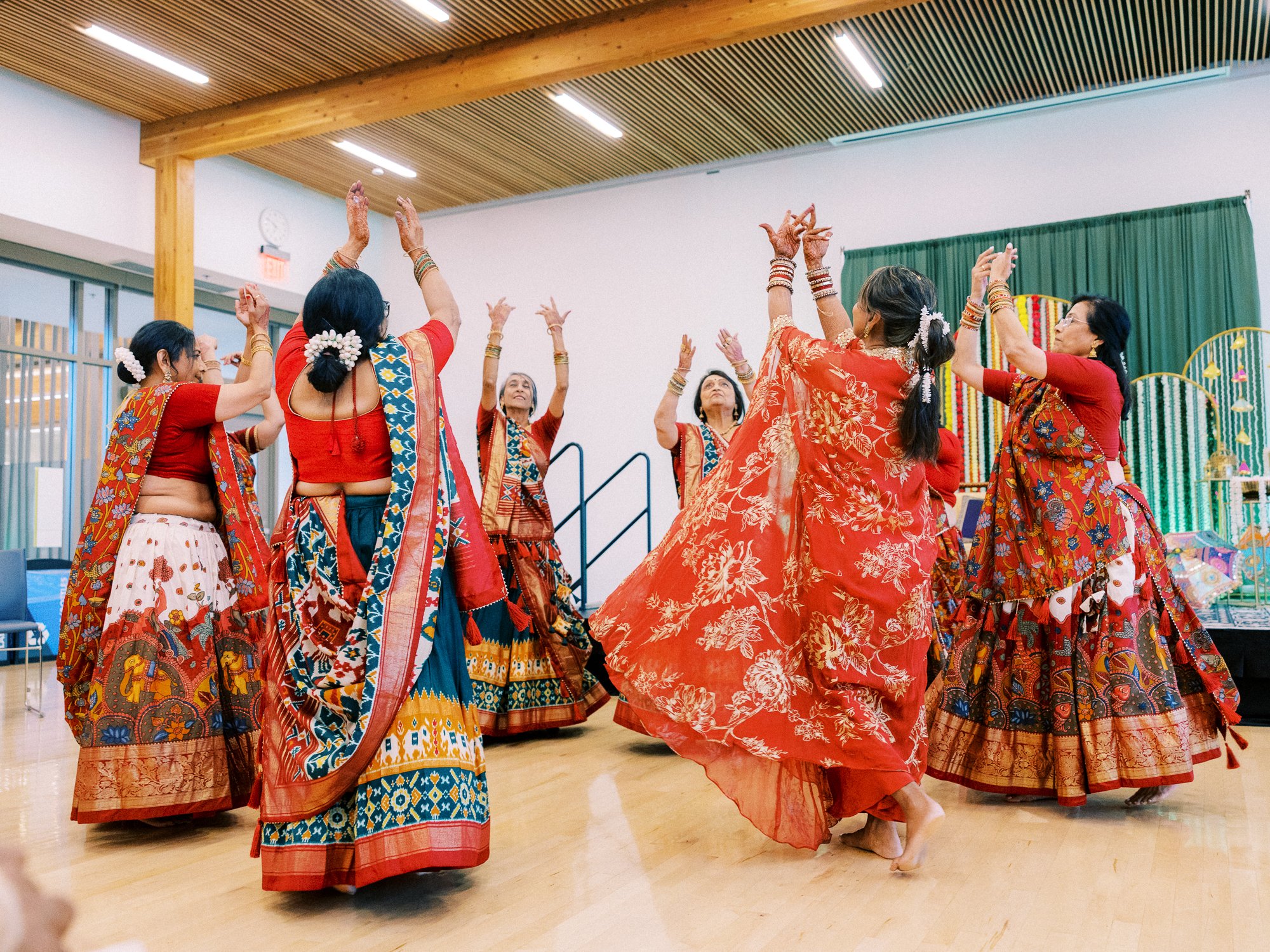 Women in vibrant red traditional outfits dance together during the Mehndi festivities.