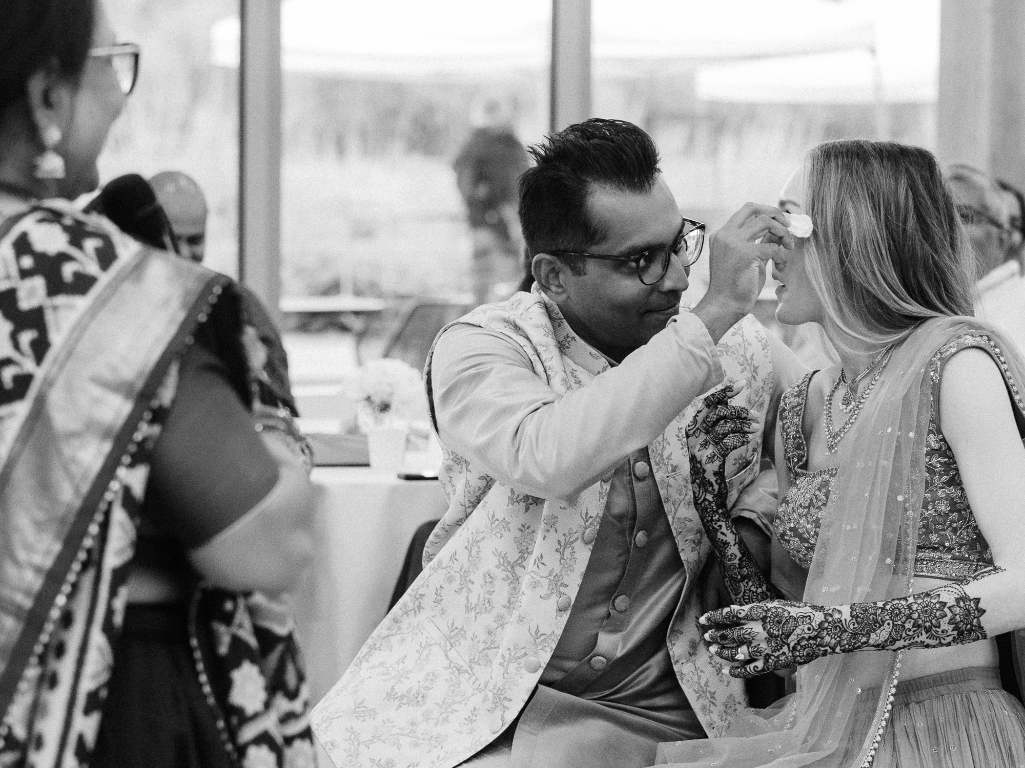 Black-and-white candid of Rohit gently wiping Alacia’s face as her detailed henna is visible.