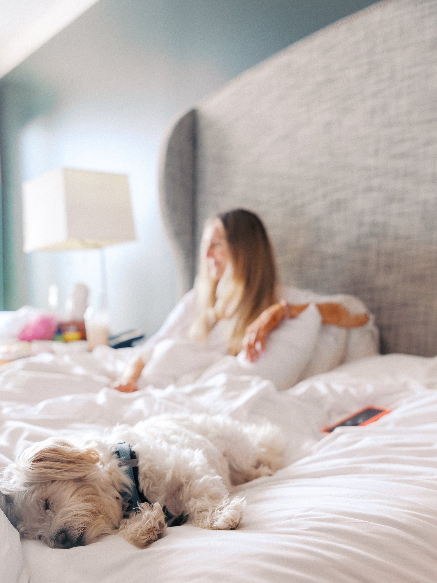 Alacia relaxing on the bed with her small white dog while getting ready at the Sentinel Hotel in Portland.