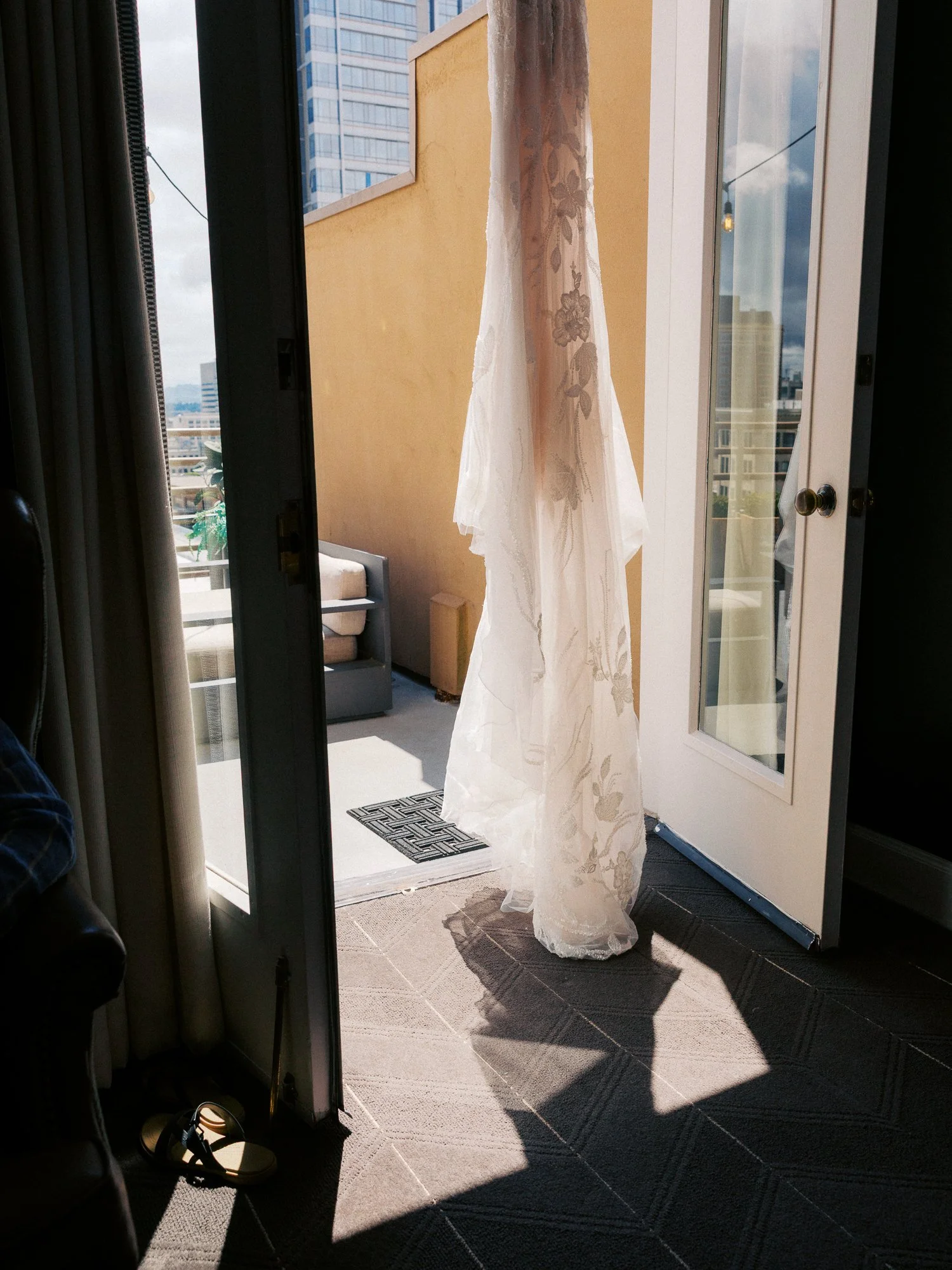 Alacia’s white wedding dress hanging in the doorway of a Sentinel Hotel room overlooking downtown Portland.