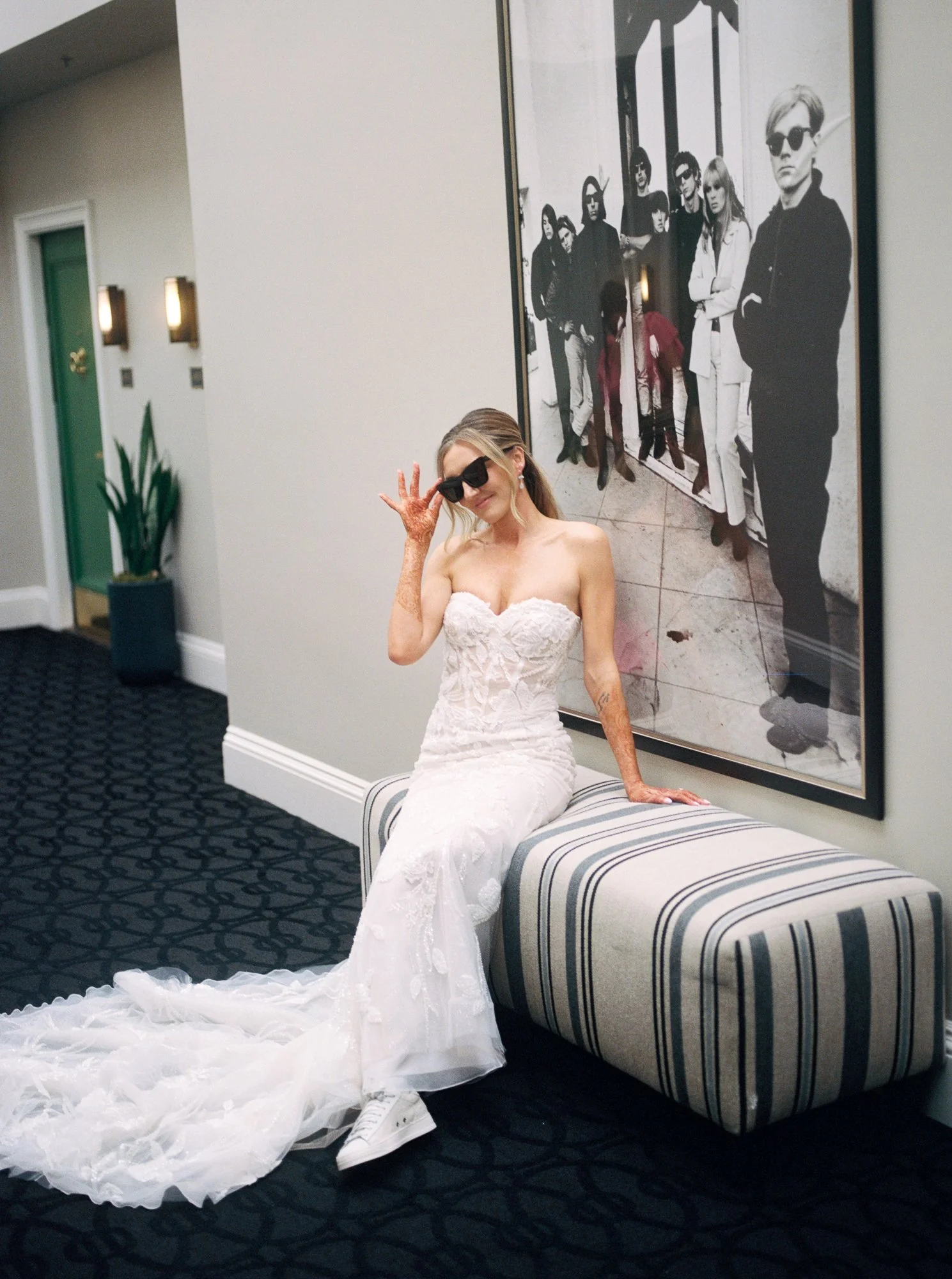 Alacia wearing sunglasses and a wedding dress while seated beneath black-and-white artwork at the Sentinel Hotel.
