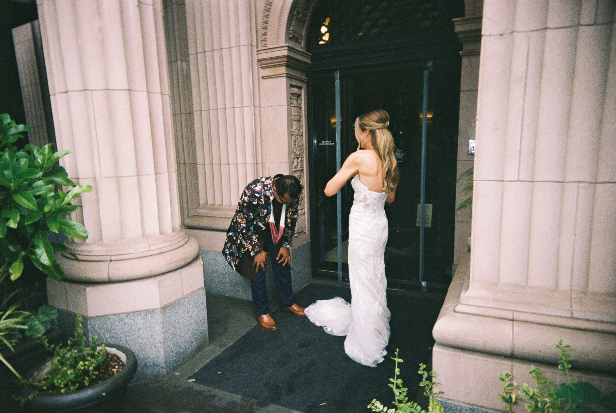 Bride waits near the ornate entrance of the Sentinel Hotel as the groom bends forward during their first look.