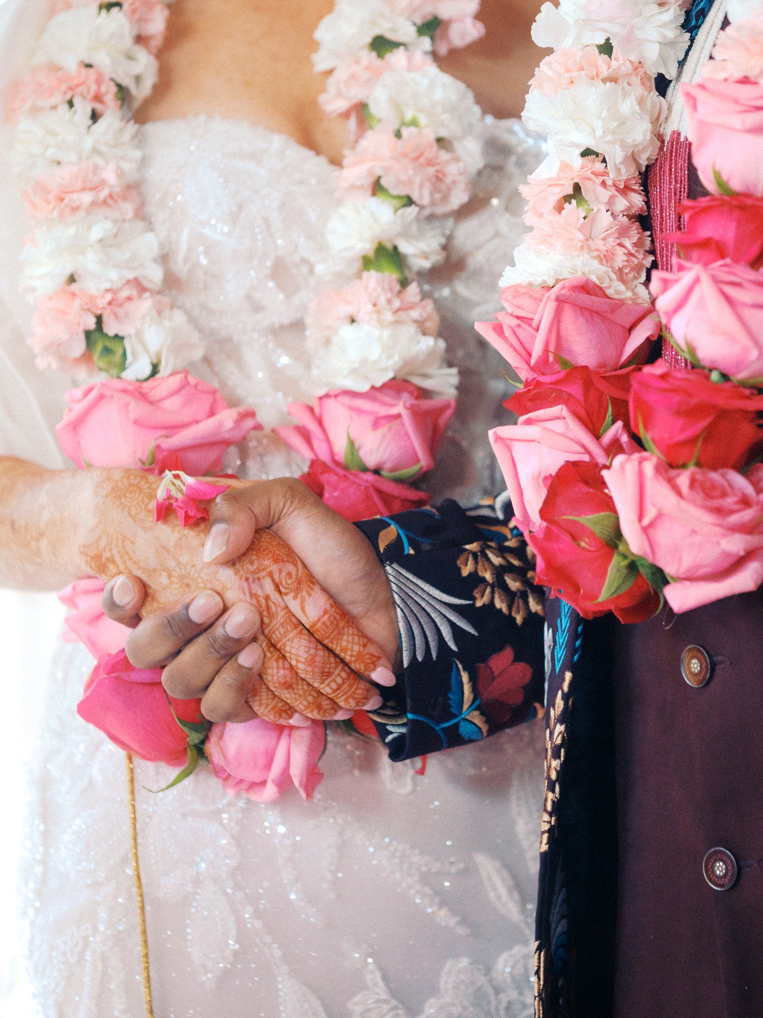 Close-up of the couple holding hands, surrounded by pink rose garlands and floral leis.