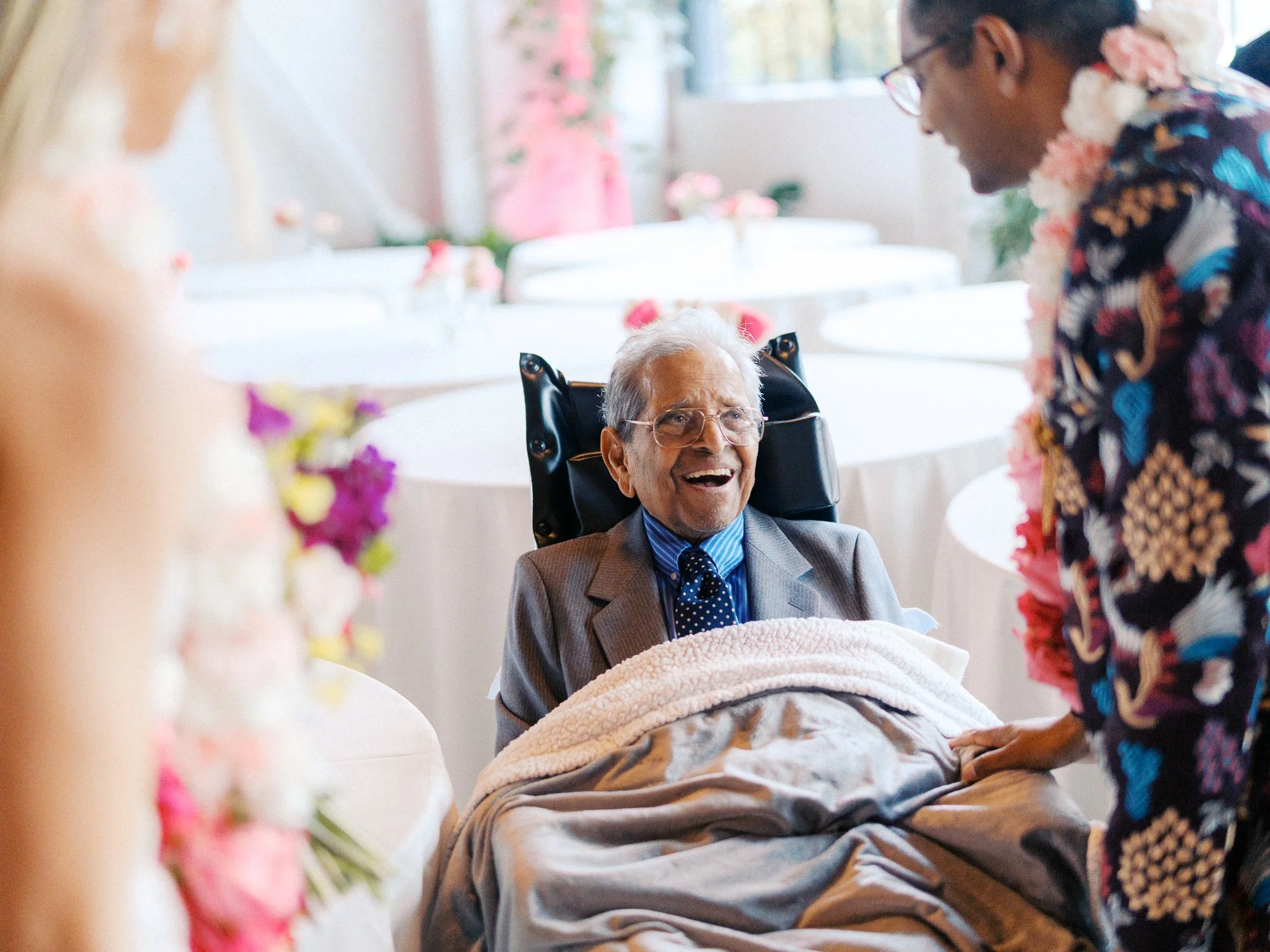 Elderly wedding guest smiles from a wheelchair as the couple greets him after the ceremony.