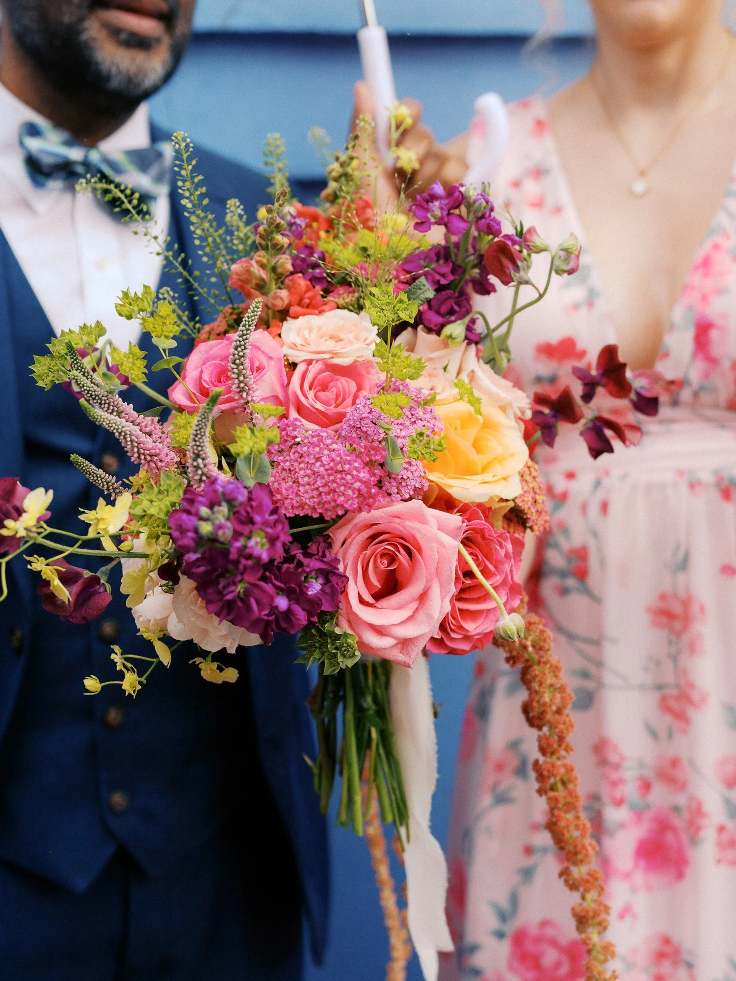 Vibrant wedding bouquet with pink, peach, yellow, and purple flowers held by guests.