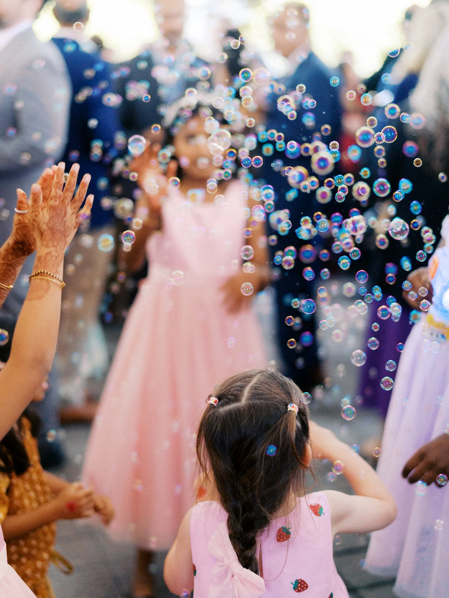 Young wedding guest watches colorful bubbles floating through the crowd.