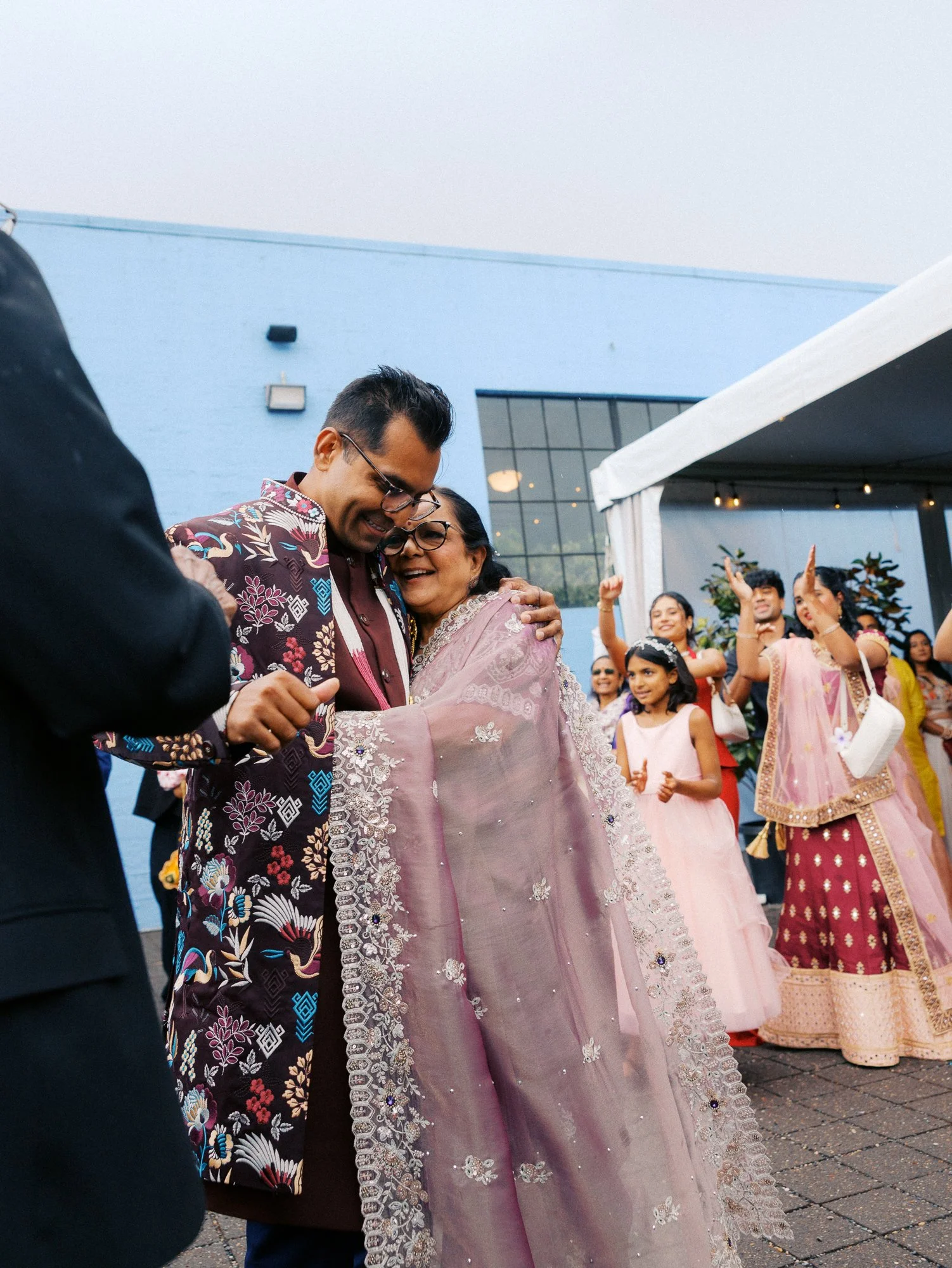 Groom embraces a woman in a lavender embroidered sari during the wedding festivities.