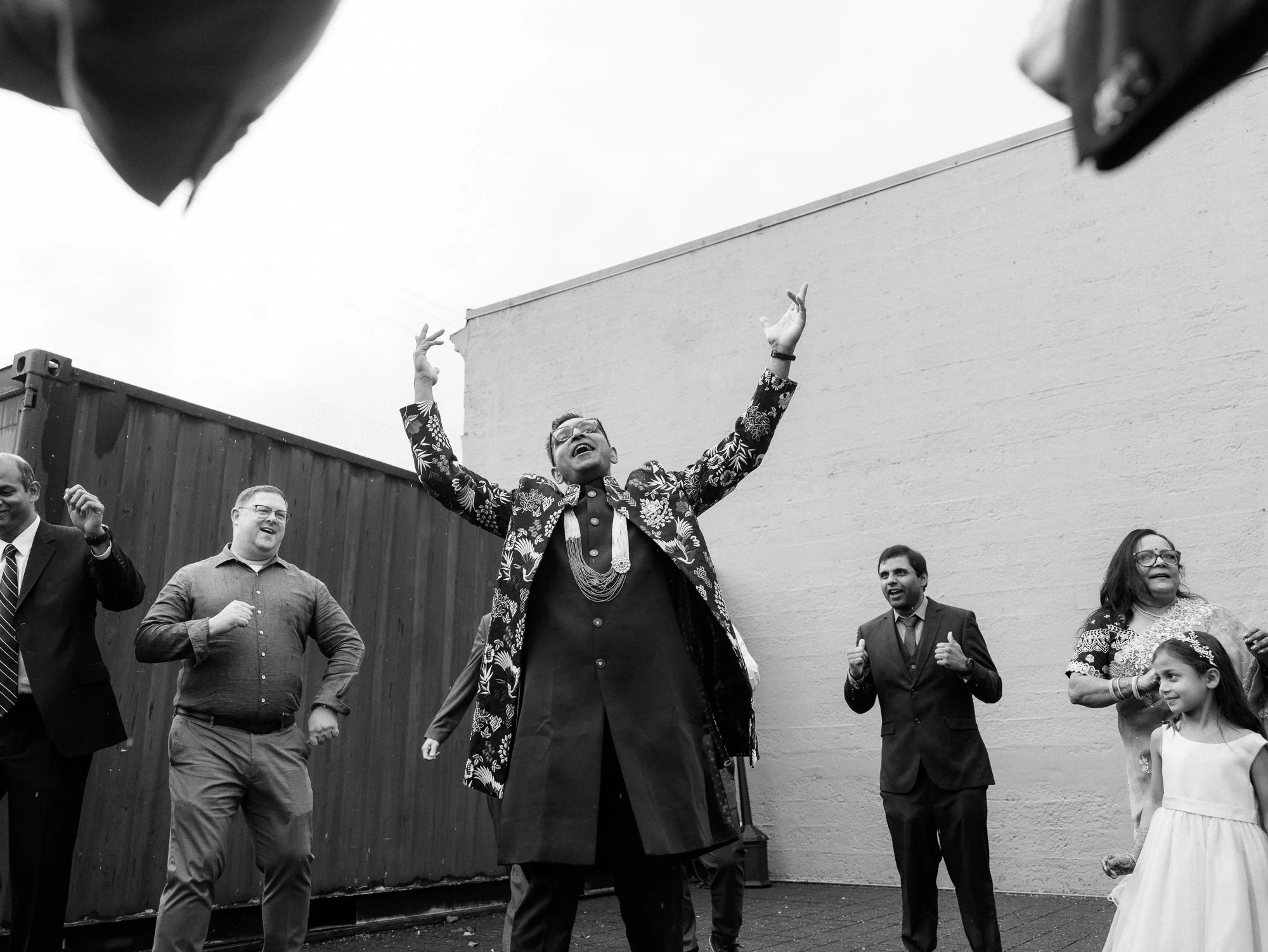 Groom raises both arms while dancing with guests outside the reception.