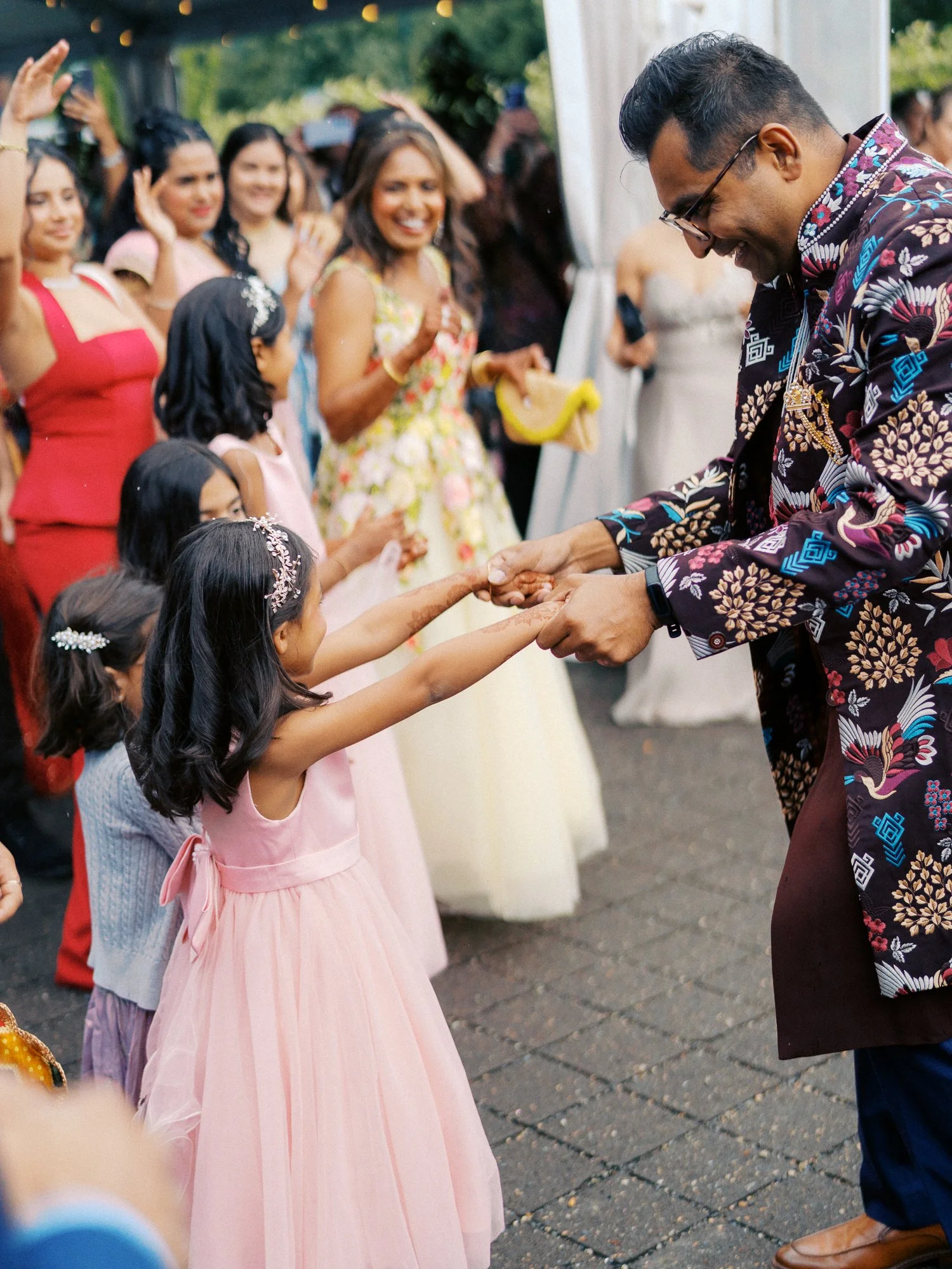 Groom holds hands and dances with a young girl in a pink dress.