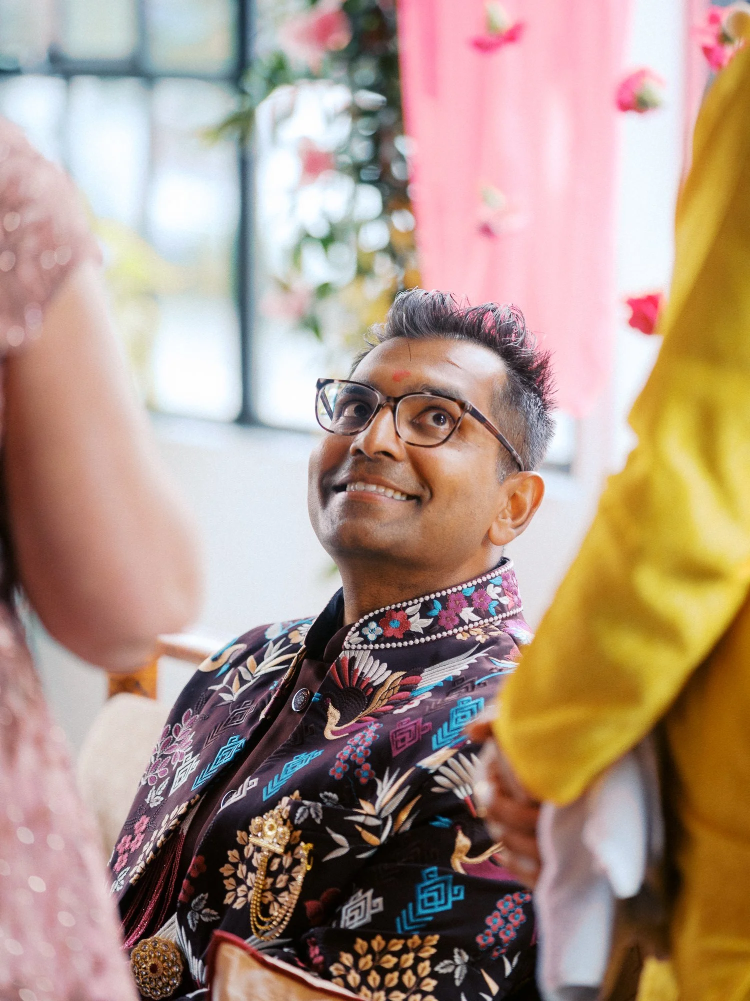 Groom in an embroidered jacket looks upward during the wedding ceremony.
