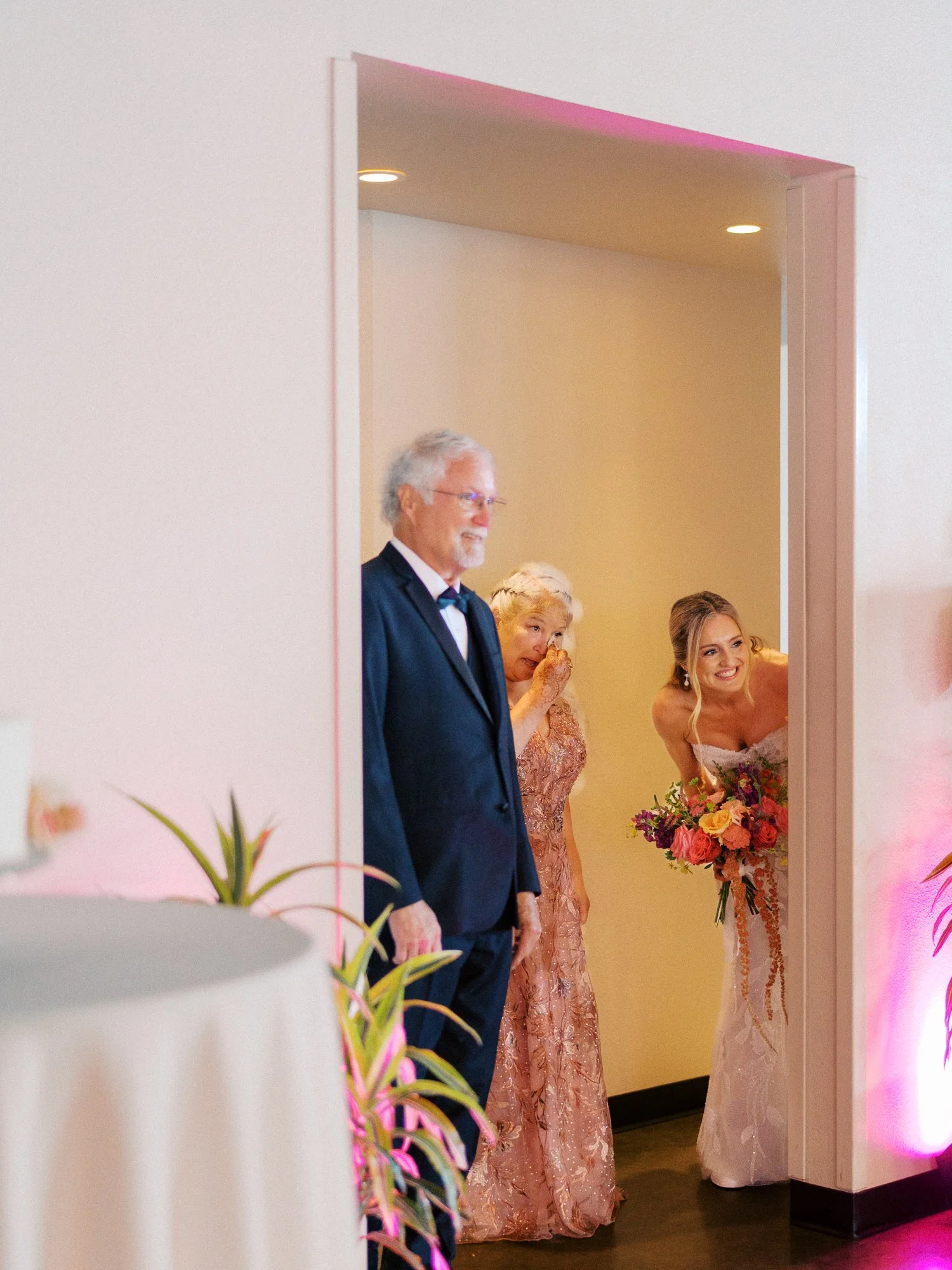 Bride waits at the ceremony entrance with two older family members and a colorful bouquet.