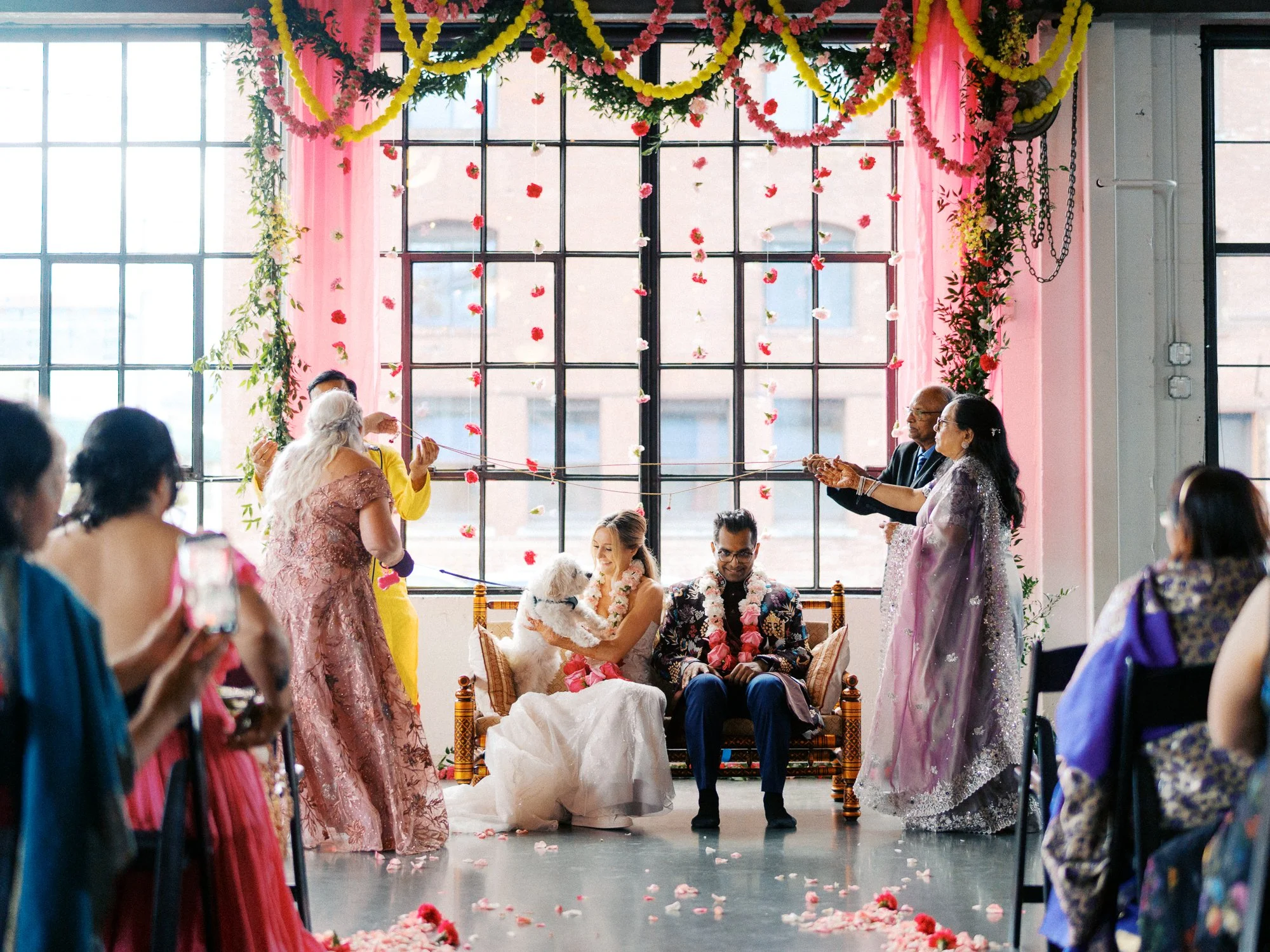 Bride and groom sit beneath hanging pink and yellow floral garlands during their ceremony at Castaway Portland.