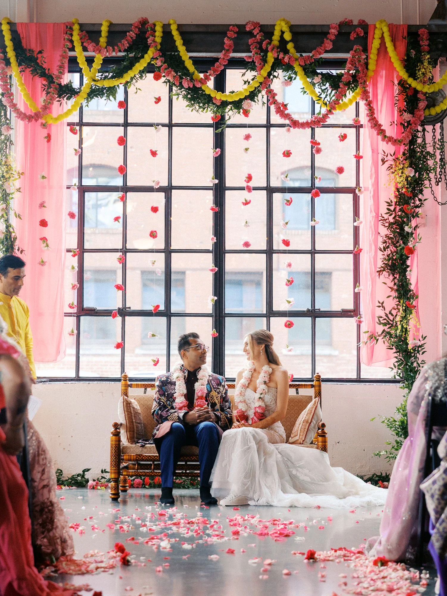 Bride and groom sit together beneath hanging flowers and greenery during their ceremony.