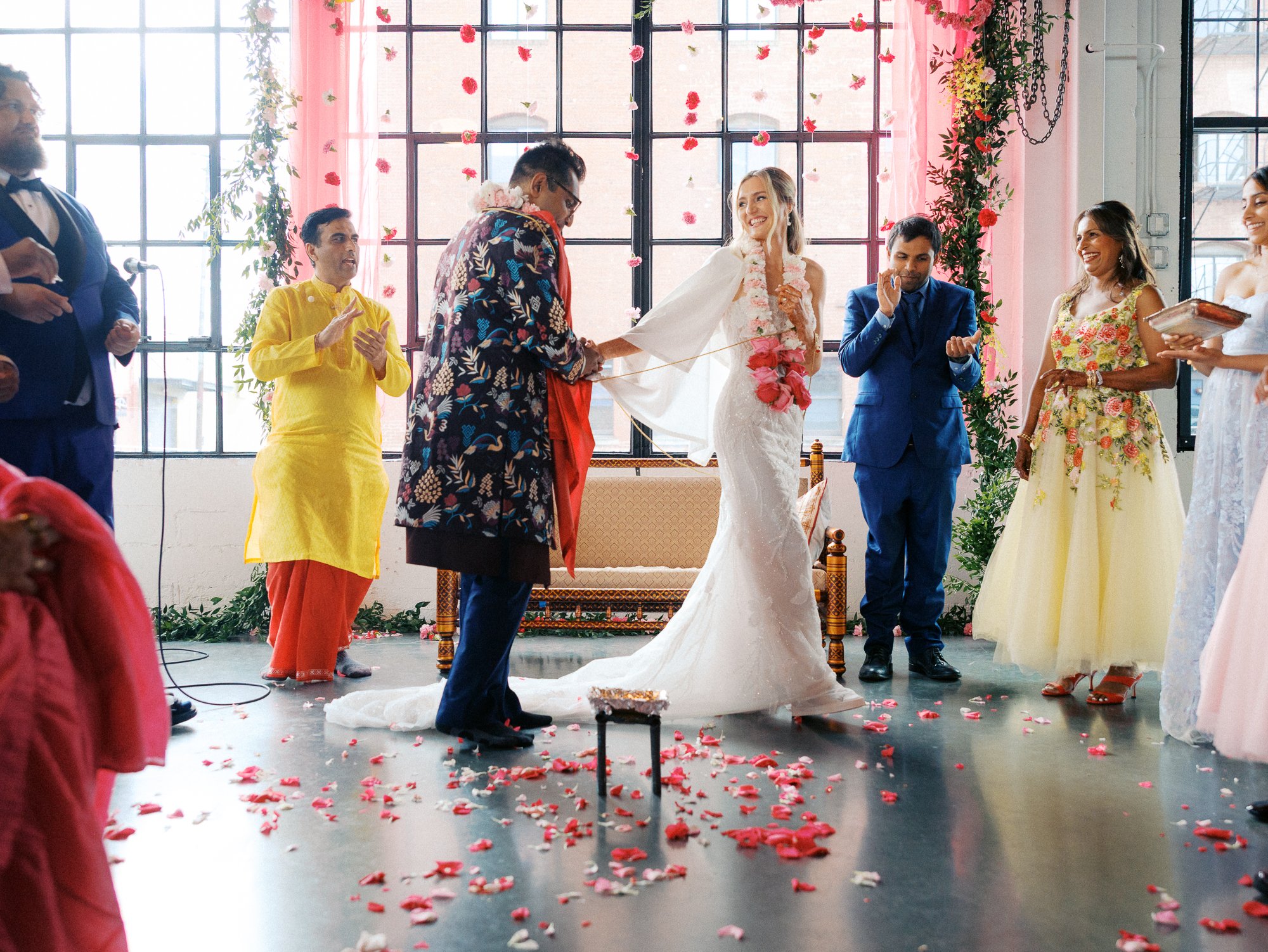 Bride and groom stand together during a traditional wedding ritual as family and attendants gather around them.