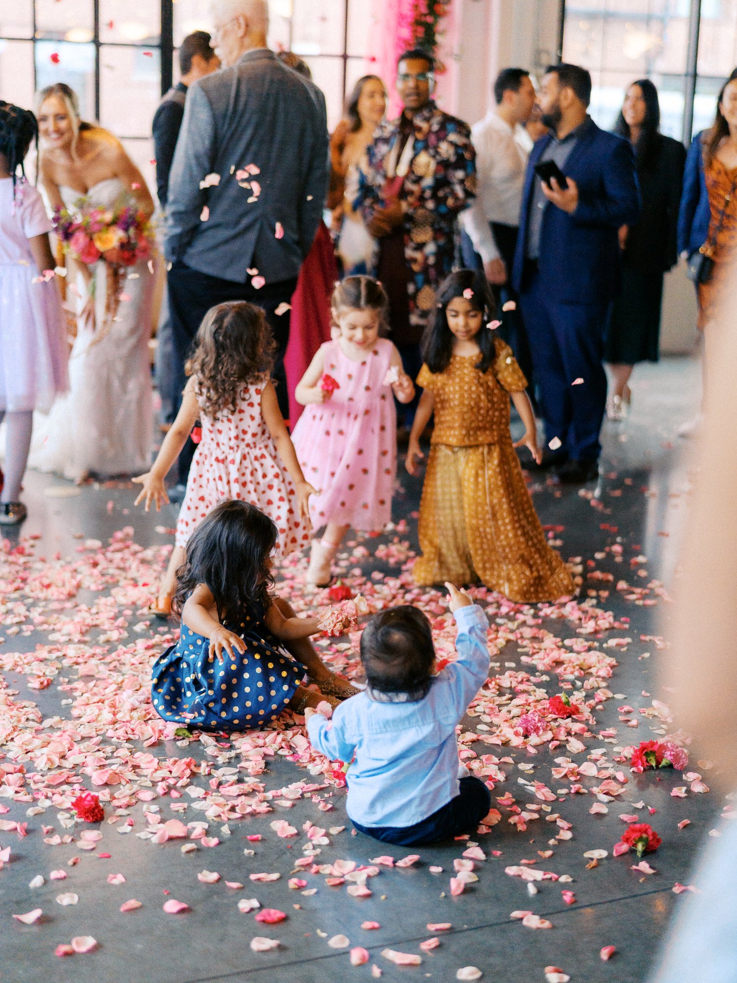 Children play among pink flower petals on the floor after the wedding ceremony.
