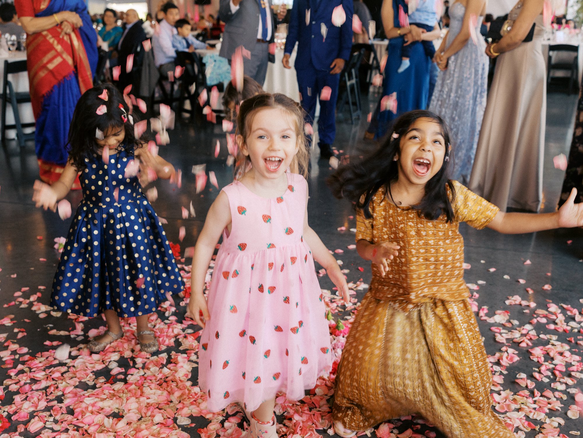 Children play on the petal-covered floor while the bride and guests mingle nearby.