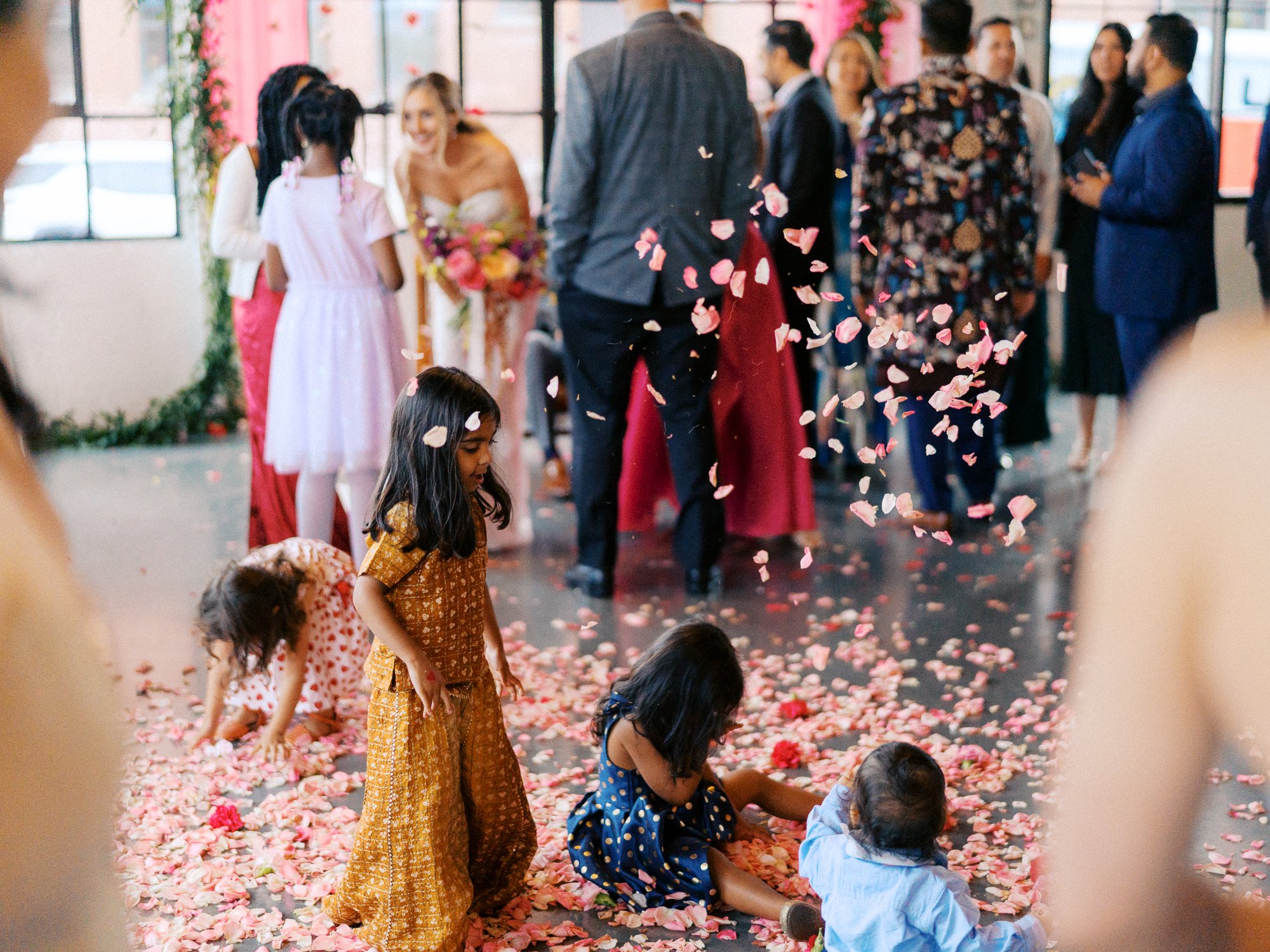 Three children laugh and play as pink petals fall around them.