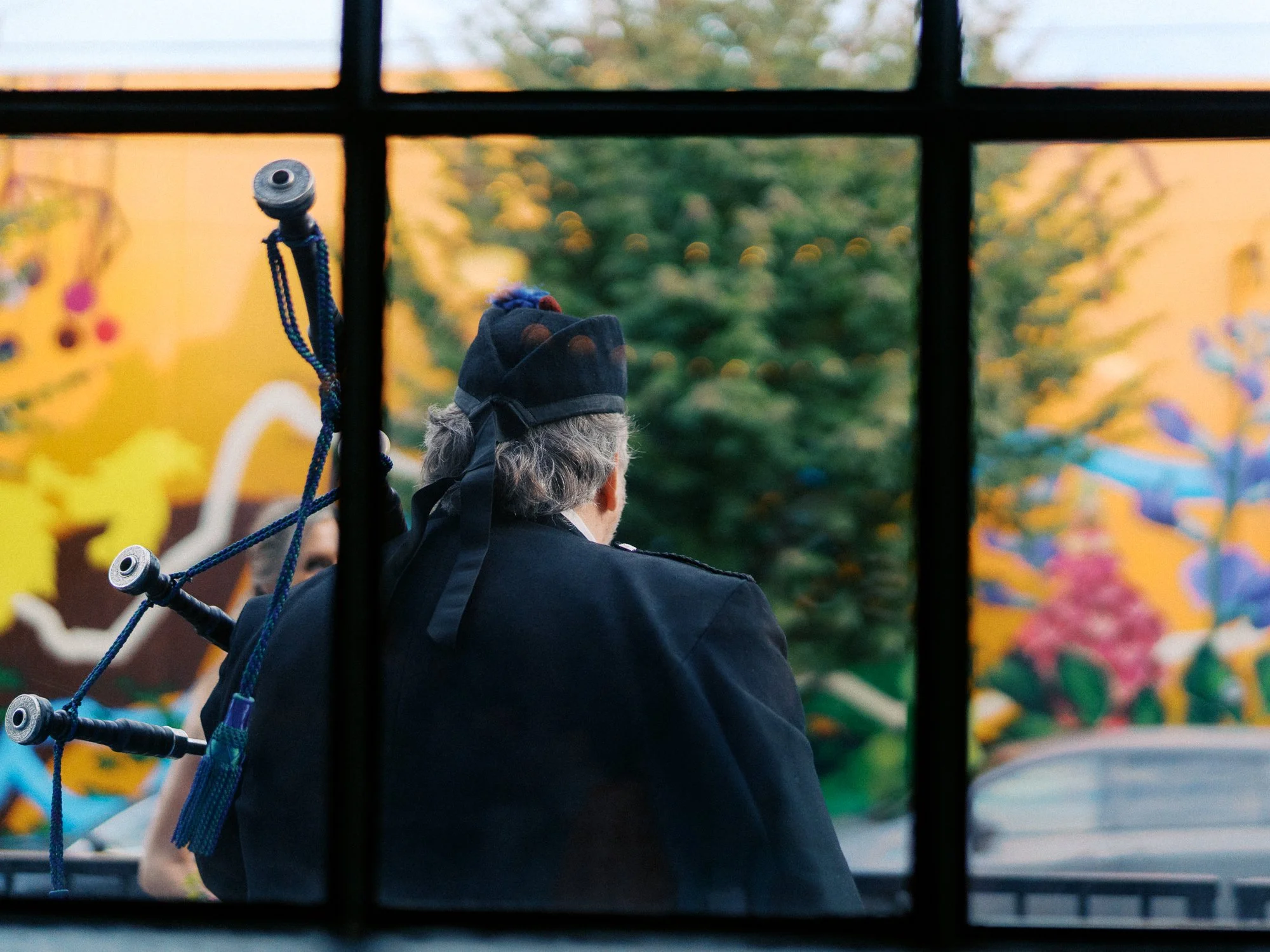 Bagpiper seen from behind through a large window outside the wedding venue.