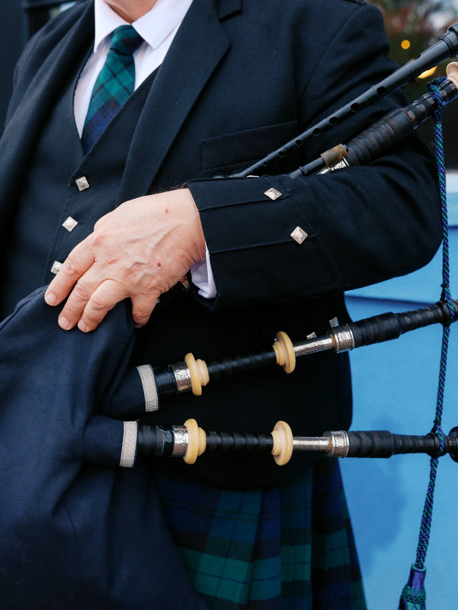 Close-up of a bagpiper in a dark jacket and green plaid kilt holding the instrument.