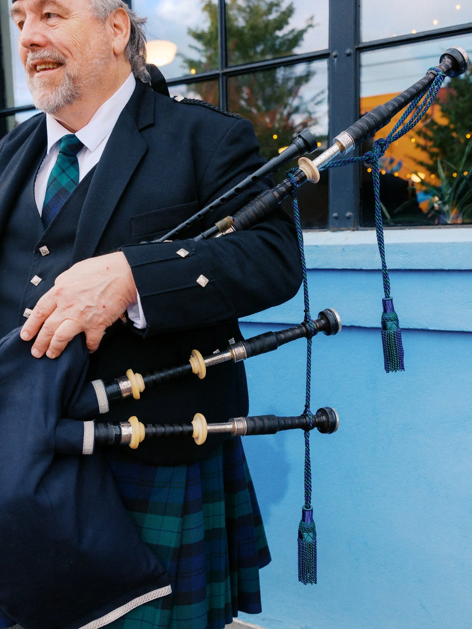 Bagpiper in formal Scottish attire holds his pipes outside Castaway Portland.