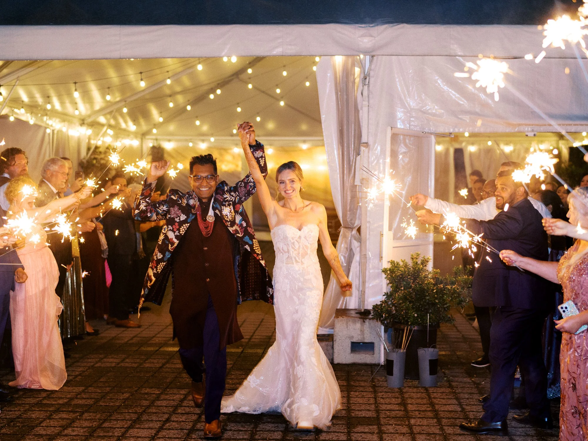 Newlyweds walk through a sparkler exit outside Castaway Portland, holding hands as guests line the path.