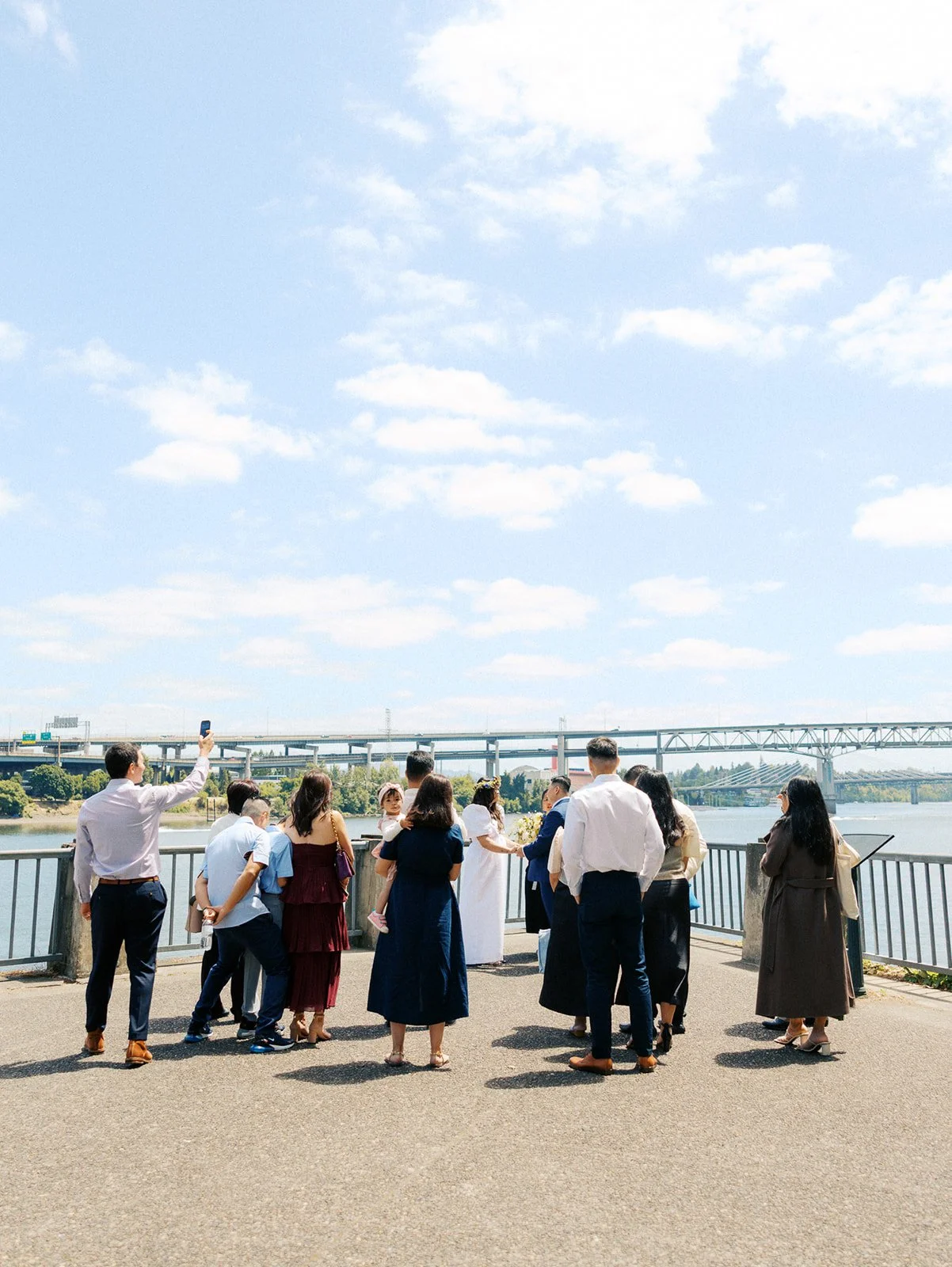 Wedding guests watch a couple exchange vows along the Portland waterfront beneath a bright blue sky.