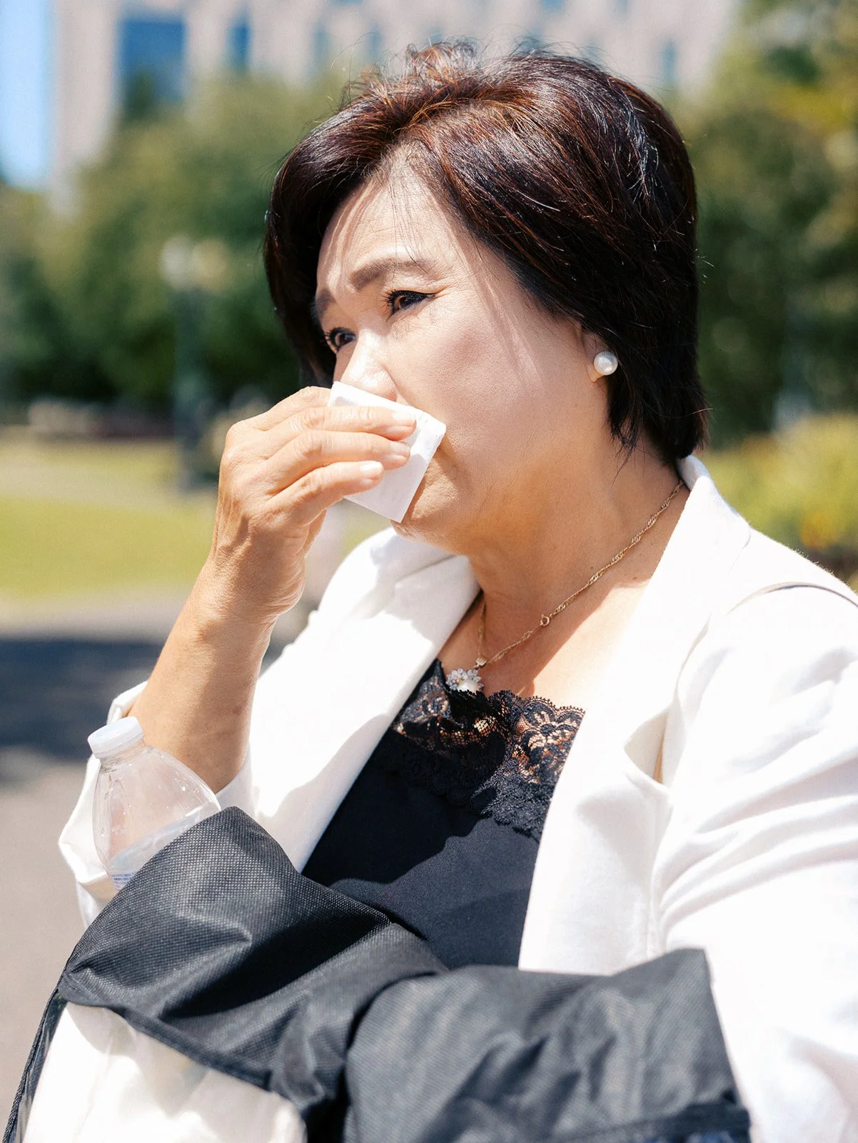 Wedding guest in a white blazer wipes her face with a tissue during an outdoor wedding celebration.