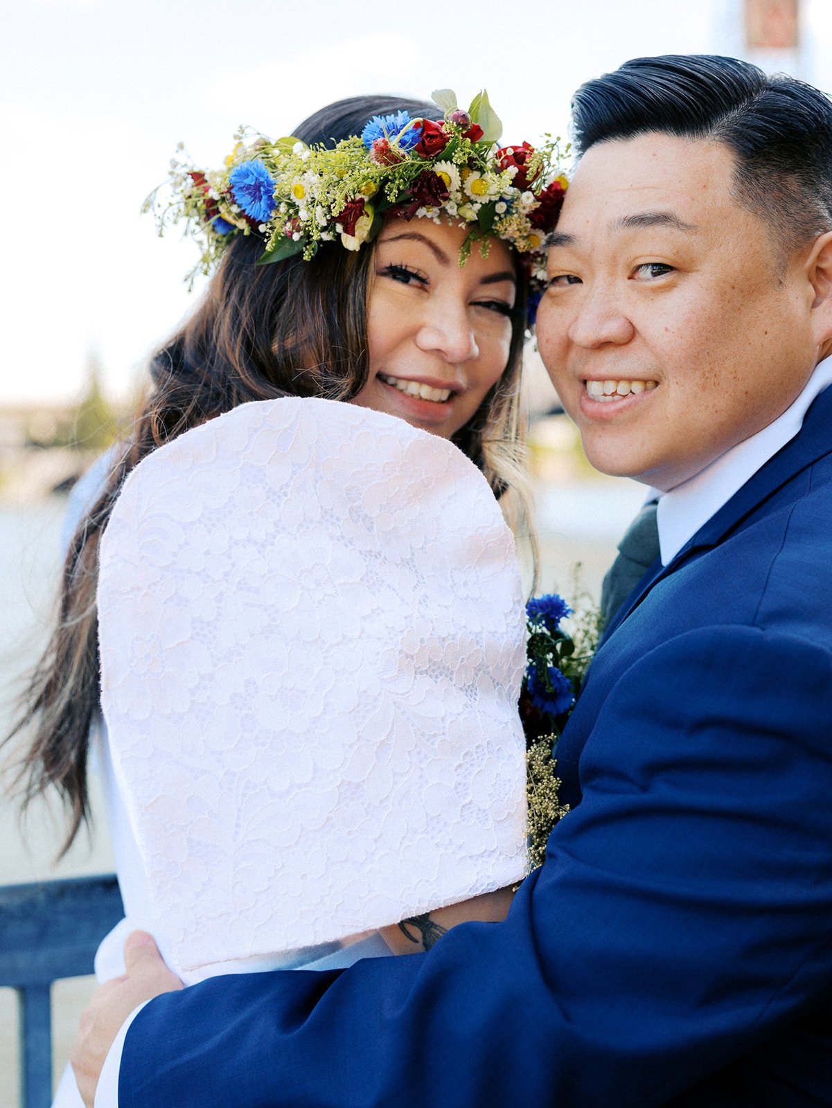 Close-up of newlyweds embracing, highlighting the bride's colorful flower crown and lace puff-sleeve wedding dress.