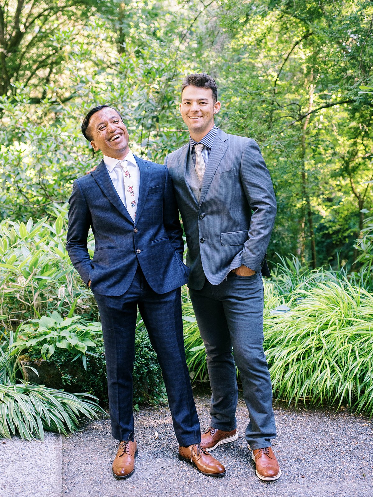 Groom poses with a groomsman on a leafy garden path after the ceremony.