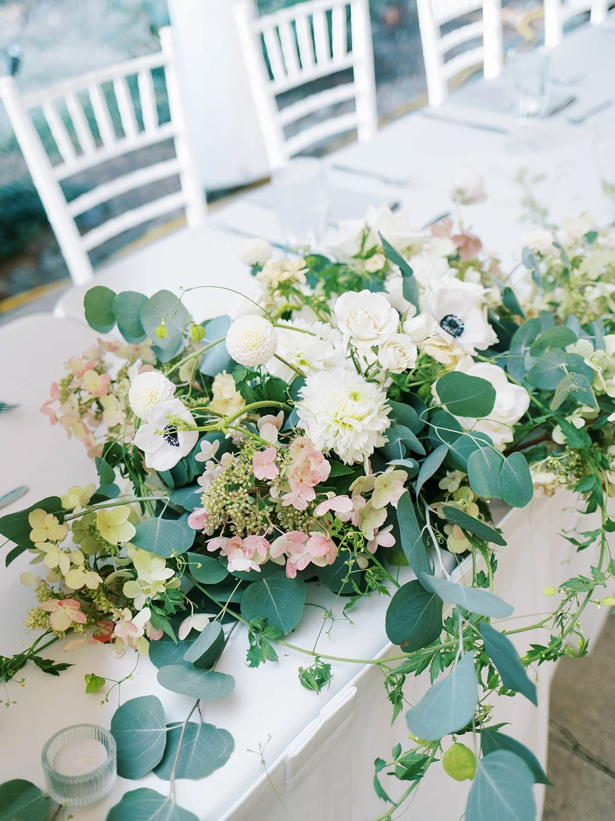 Elegant wedding reception table centerpiece with white, blush, and green florals cascading across a white table.