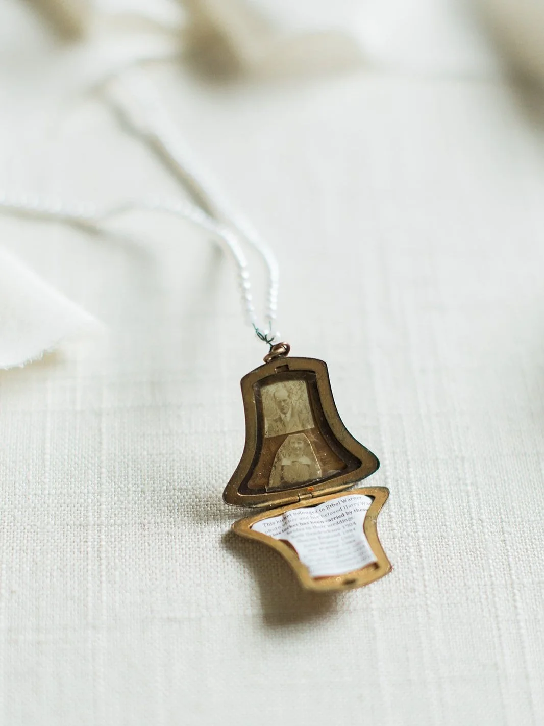 Open vintage photo locket with small family portraits displayed on white fabric.
