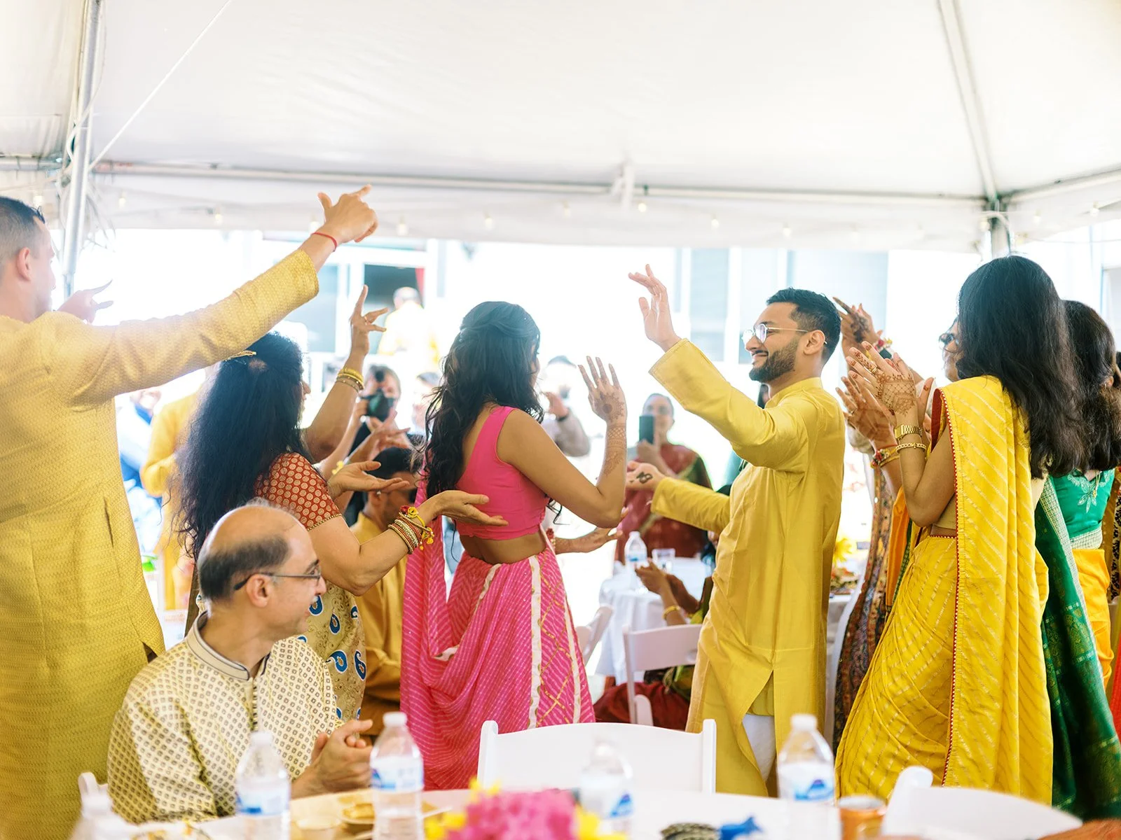 a group of people dressed in traditional yellow indian attire dancing and celebrating at a haldi ceremony