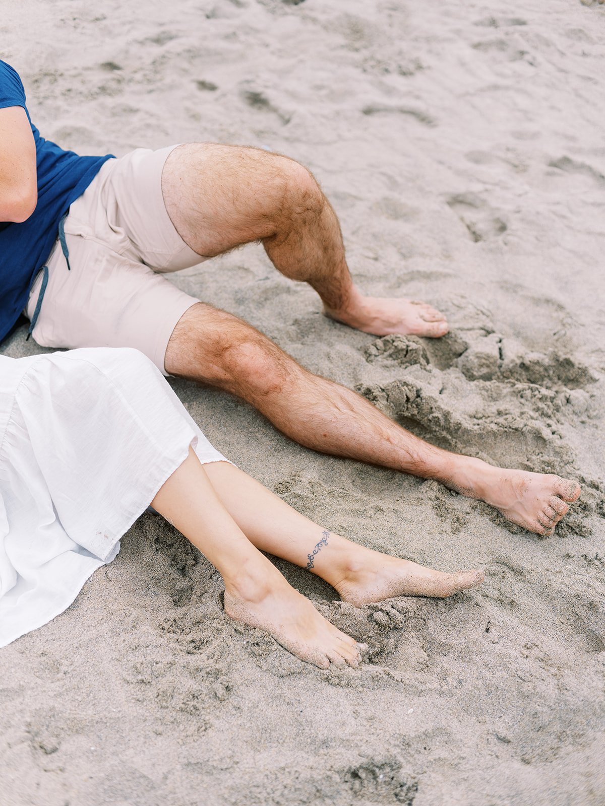 Close-up of couple’s bare feet resting together in soft beach sand.