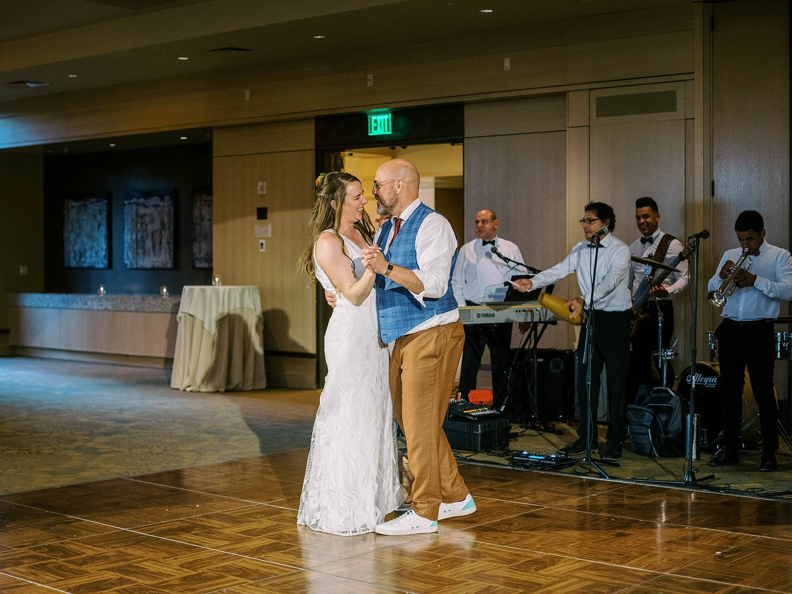 Bride and groom smiling at each other during their first dance with the live band visible behind them