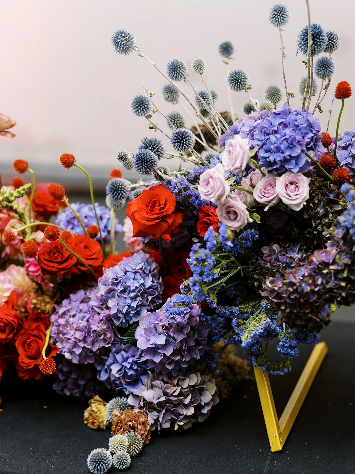 Close-up of vibrant floral arrangement with roses, hydrangeas, and spiky blue thistles on display stand.
