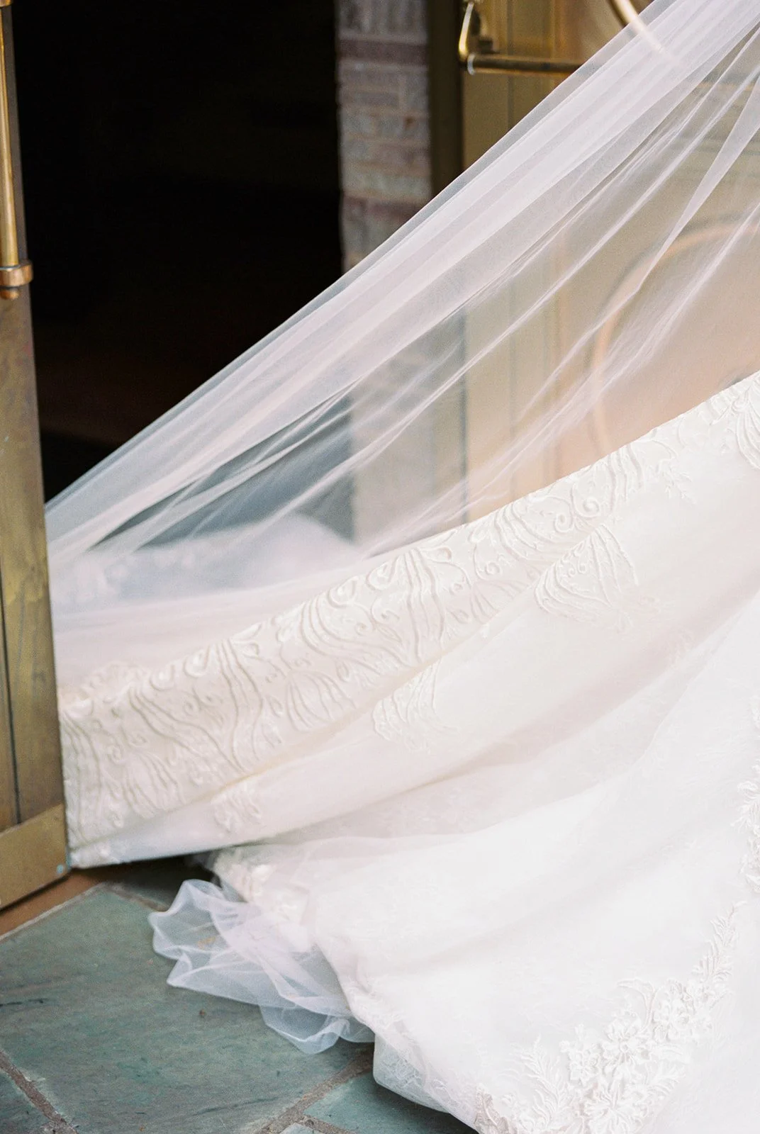 Close detail shot of the bride's lace cathedral train and sheer veil layered over the stone threshold at The Grotto's gold chapel doors