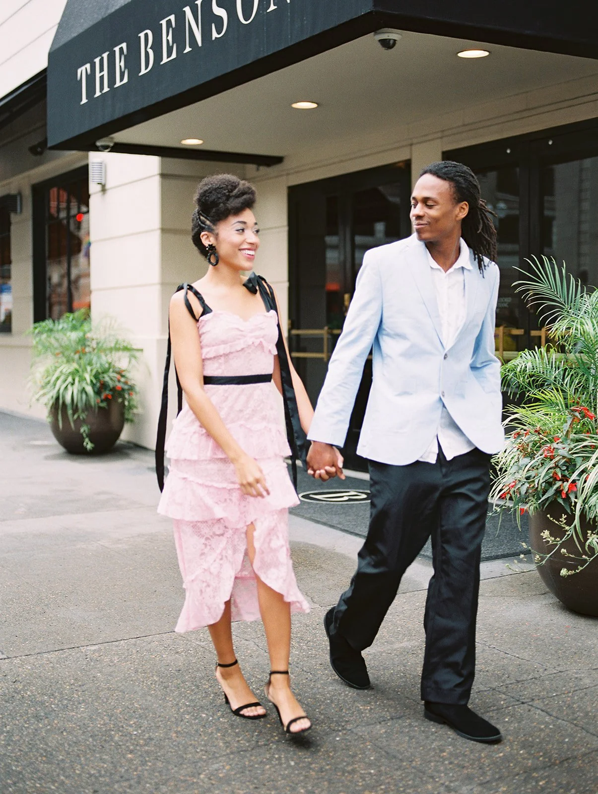 Couple walking hand in hand outside The Benson Hotel in Portland, woman in pink lace dress