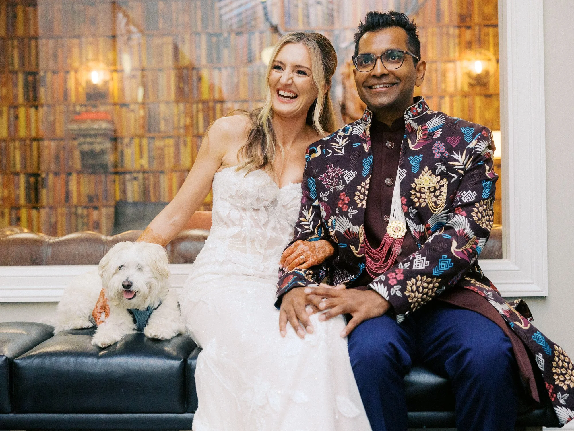 Bride and groom sit with their small white dog before heading to their wedding celebration.