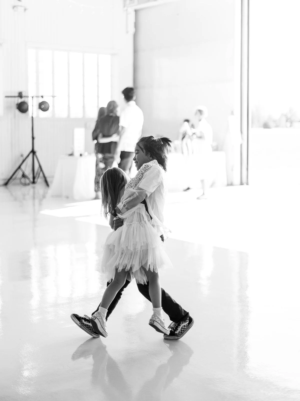 Black and white image of two young children dancing together joyfully on the polished hangar floor at the reception
