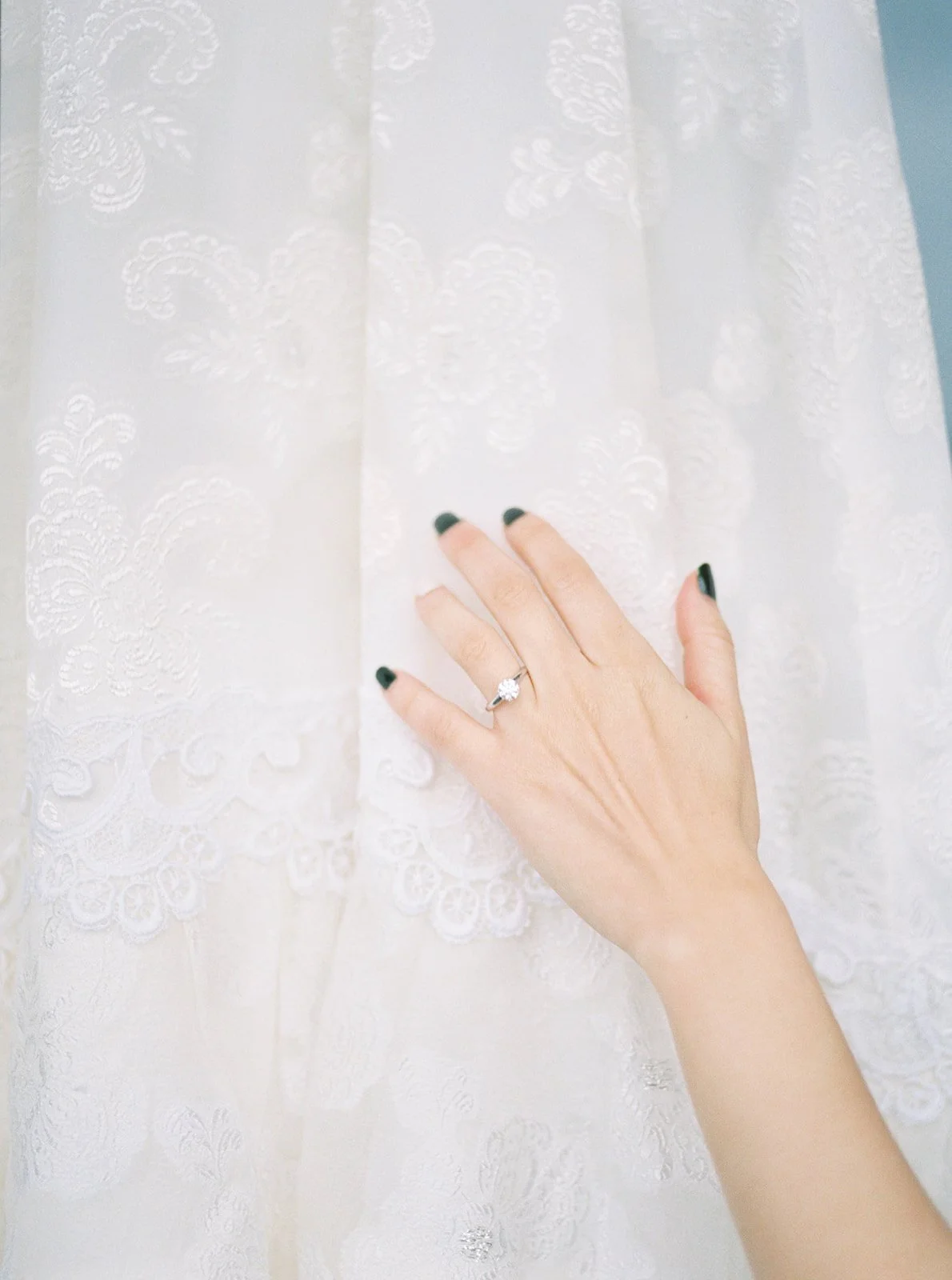 Bride’s hand with engagement ring resting against the lace detail of her vintage wedding gown.