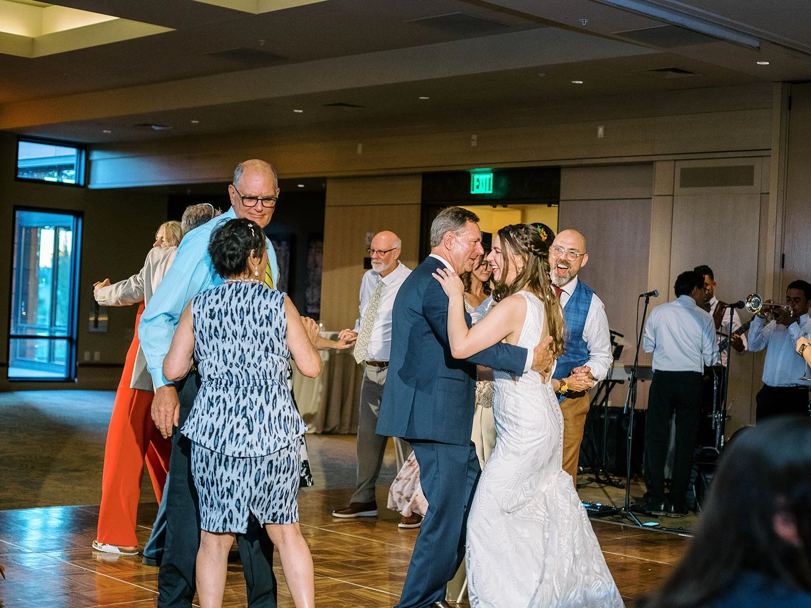 Bride dancing with a family member on the packed dance floor while the groom dances nearby and the live band plays