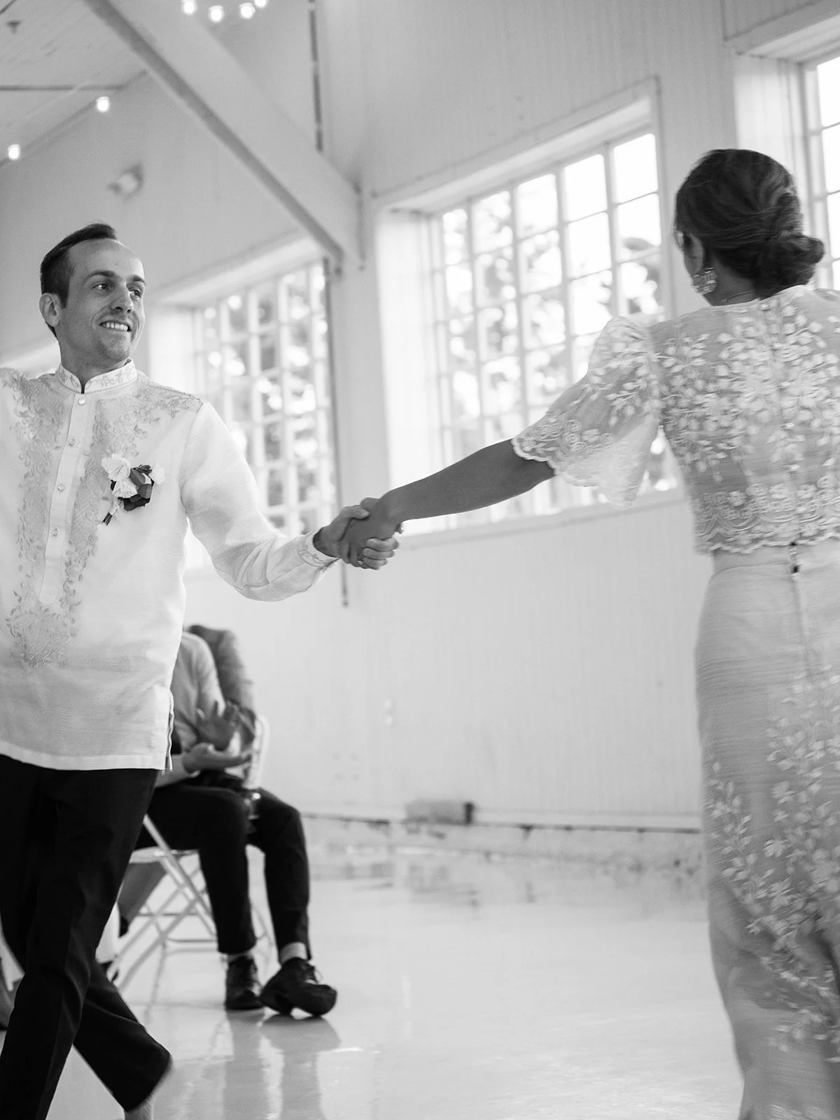 Black and white image of the groom smiling while holding the bride's hand mid-spin during their first dance inside the Pearson Air Museum hangar
