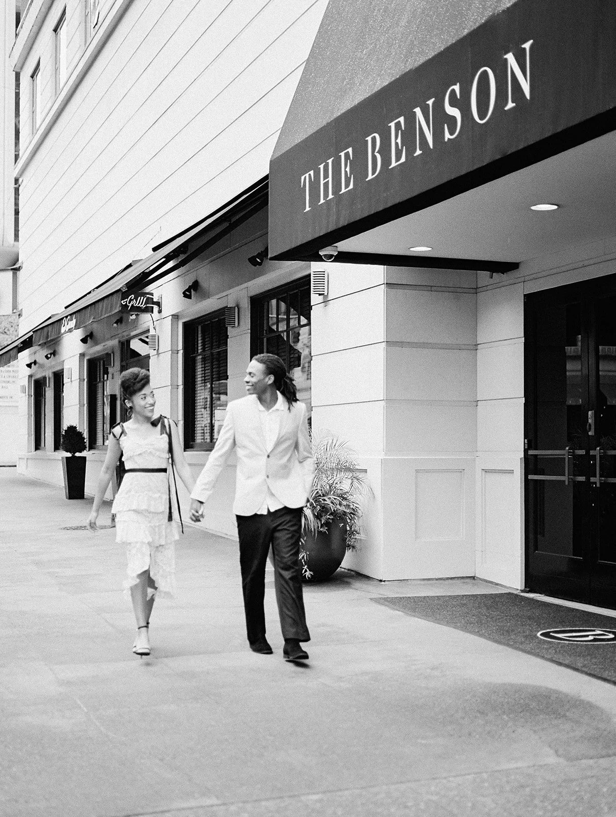 Black and white photo of couple walking past The Benson Hotel entrance in downtown Portland