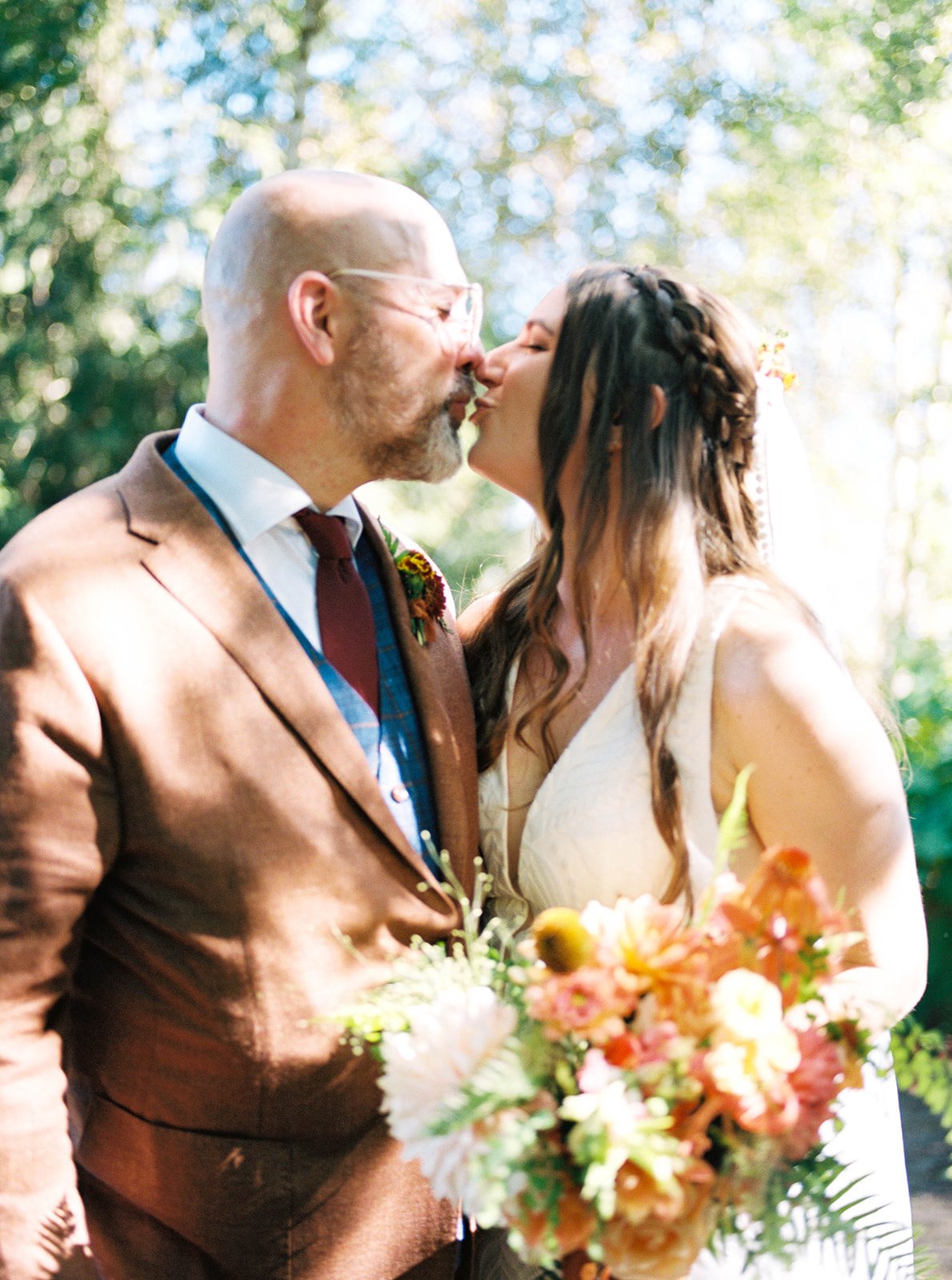 Newlyweds kissing outdoors while holding a colorful bouquet at The Allison Inn & Spa in Oregon wine country.