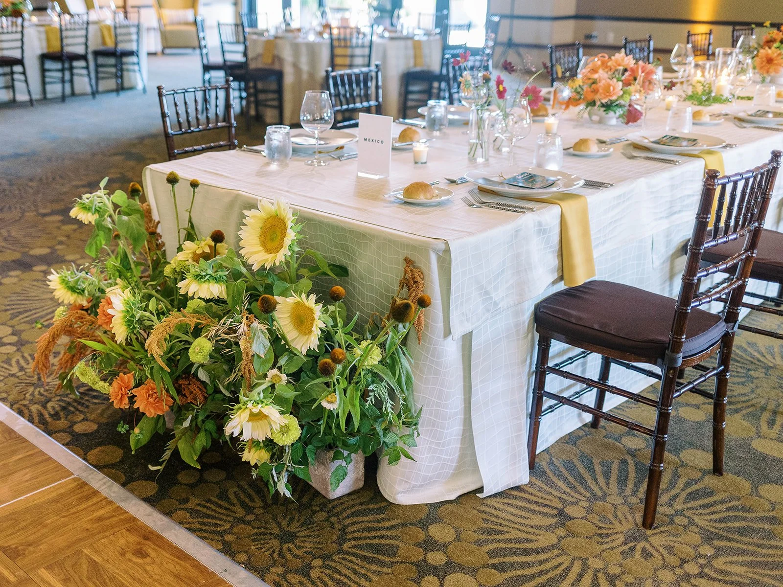 Reception table at The Allison Inn with sunflower, orange and green floral arrangements and white linens.