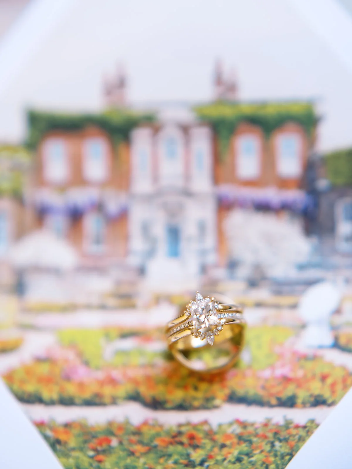 Diamond engagement ring standing upright on illustrated Sentinel Hotel artwork with soft garden background blur.