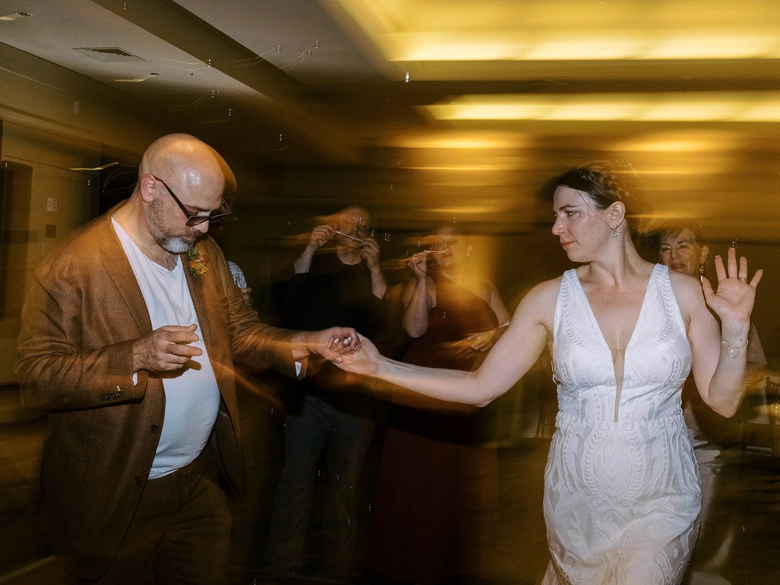 Bride and groom dancing together with motion blur, bubbles floating around them as guests blow bubbles in the background