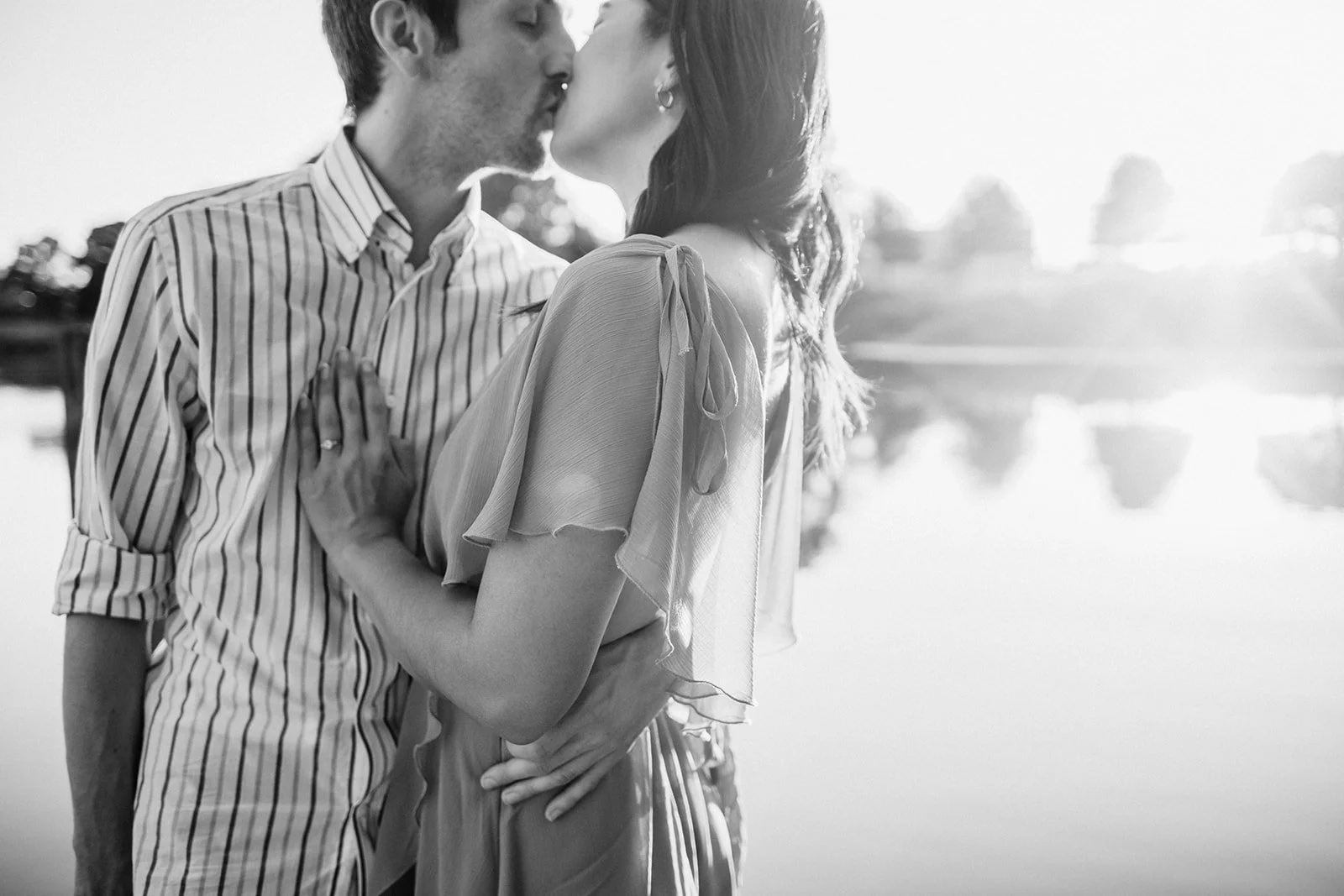Couple embracing near the lake in black and white, soft reflections behind them