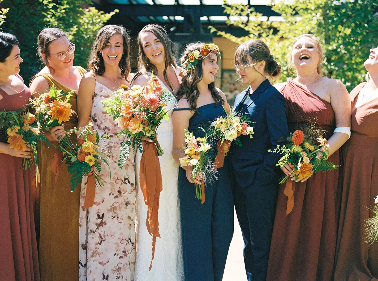 Bridesmaids and couple laughing together holding bouquets in sunny garden setting