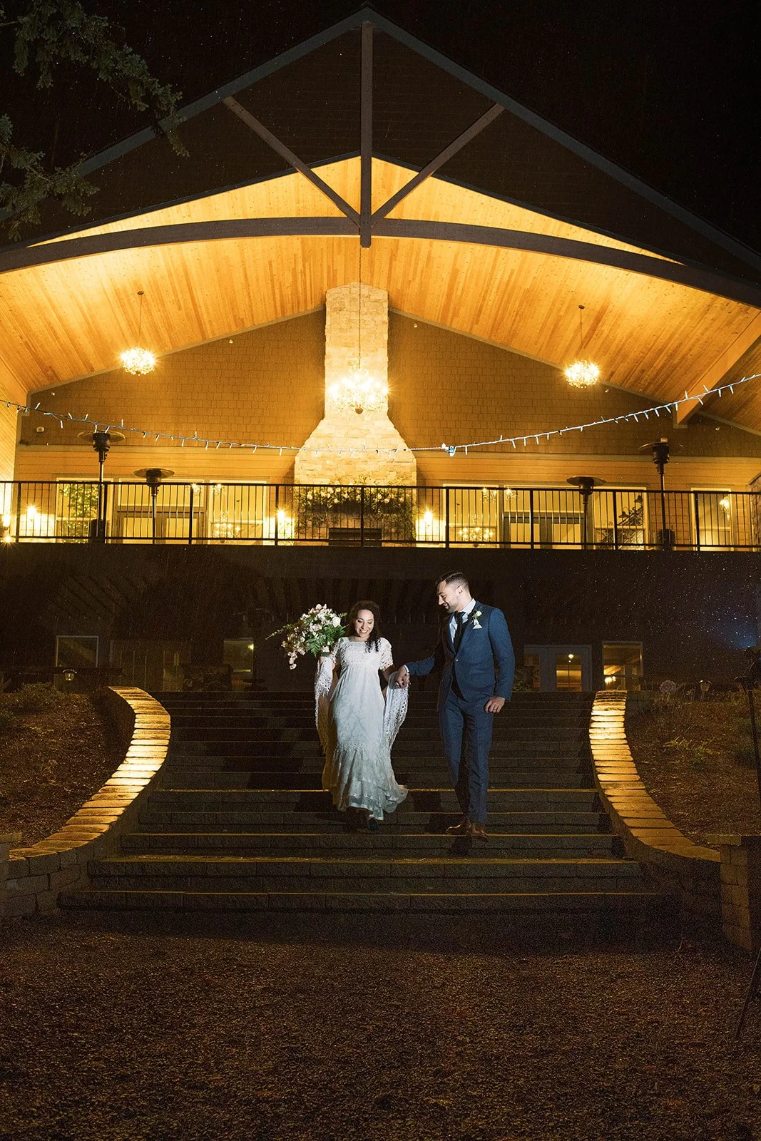 Bride and groom walk down illuminated steps beneath a glowing pavilion during their Oregon wedding at night